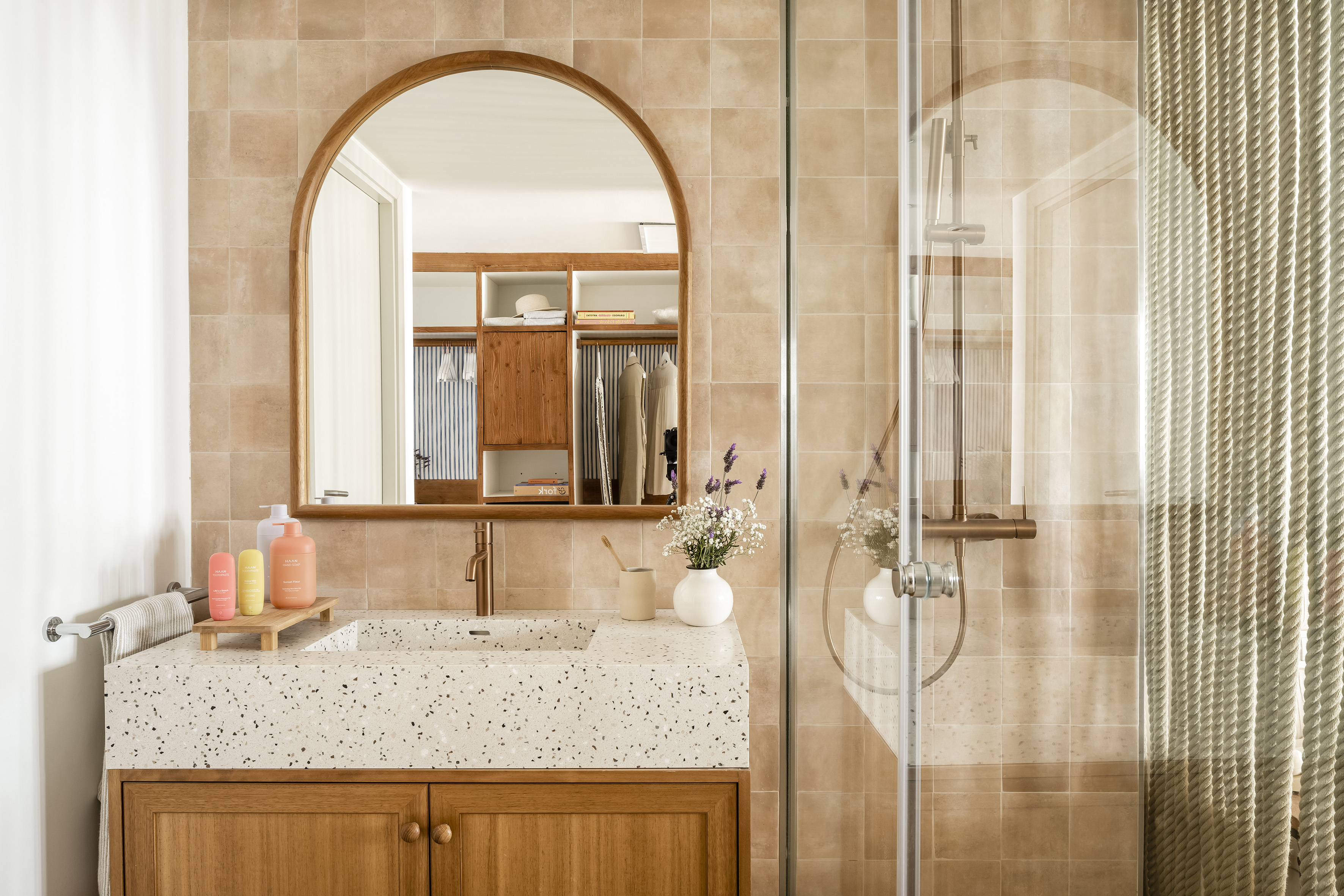 Modern bathroom with arched mirror, terrazzo vanity, and glass shower.