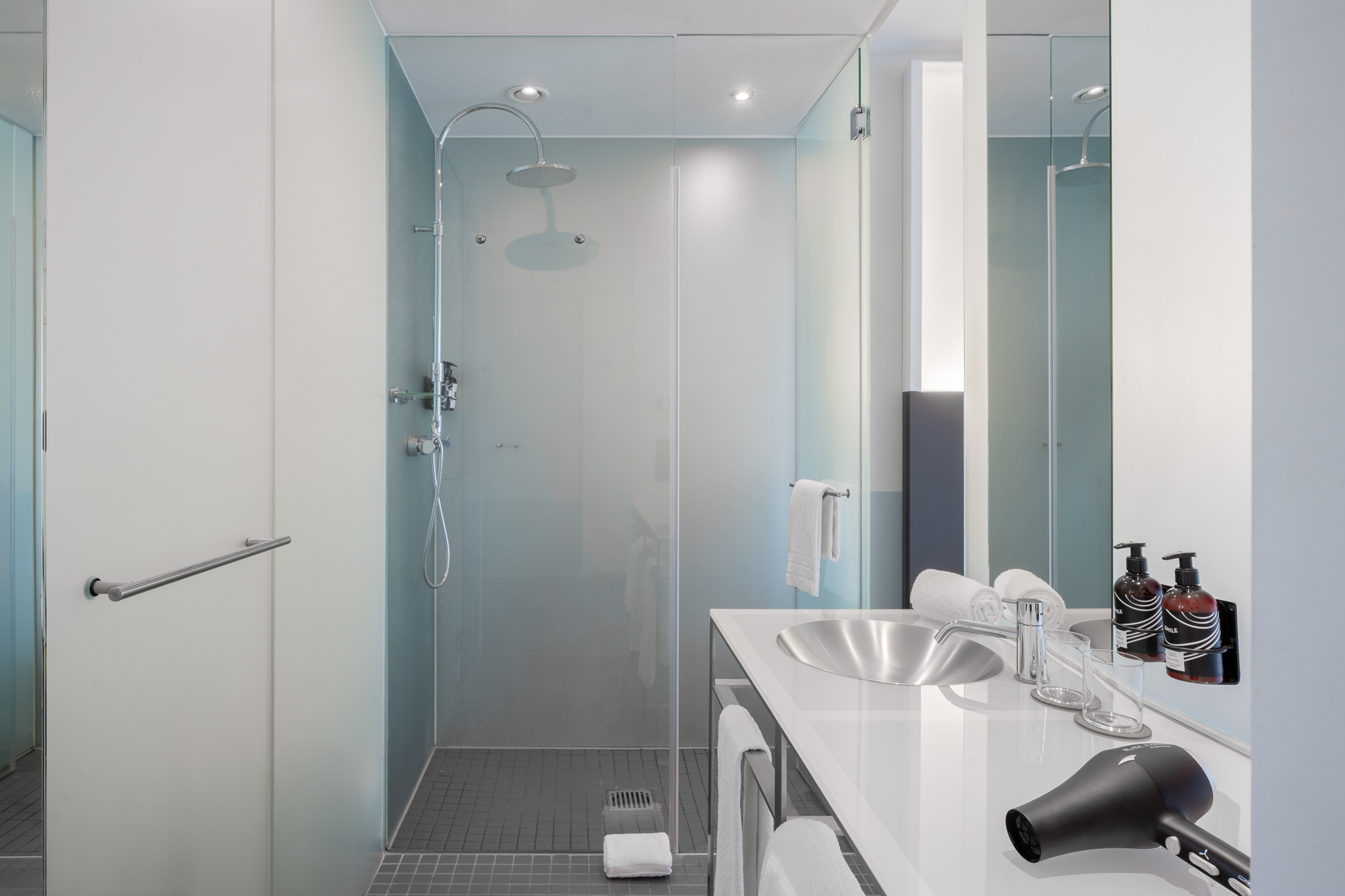 Modern bathroom with walk-in rain shower, glass partition, vanity, hairdryer.