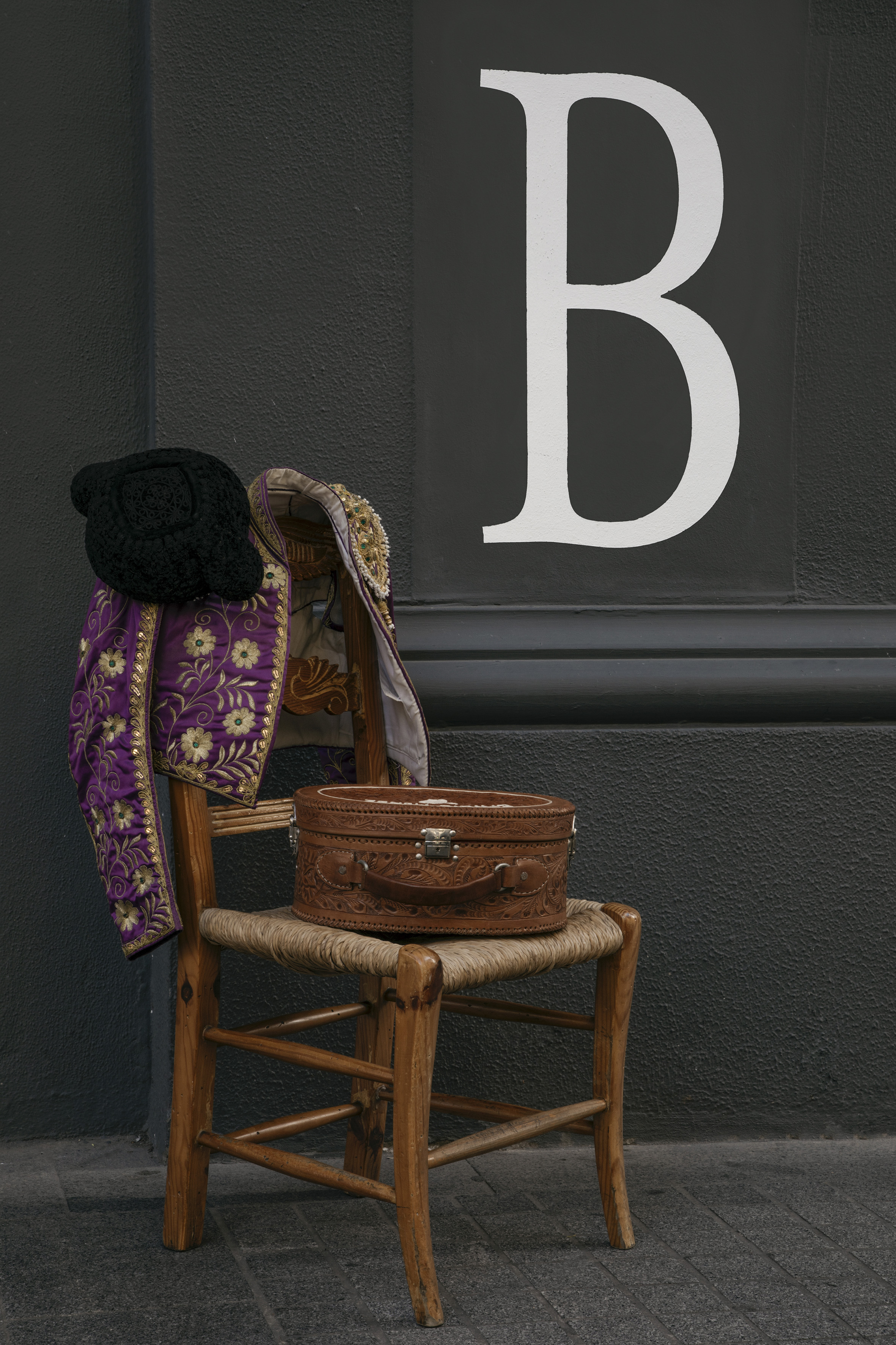 Purple matador jacket, montera, and vintage leather box on chair by 'B' wall.