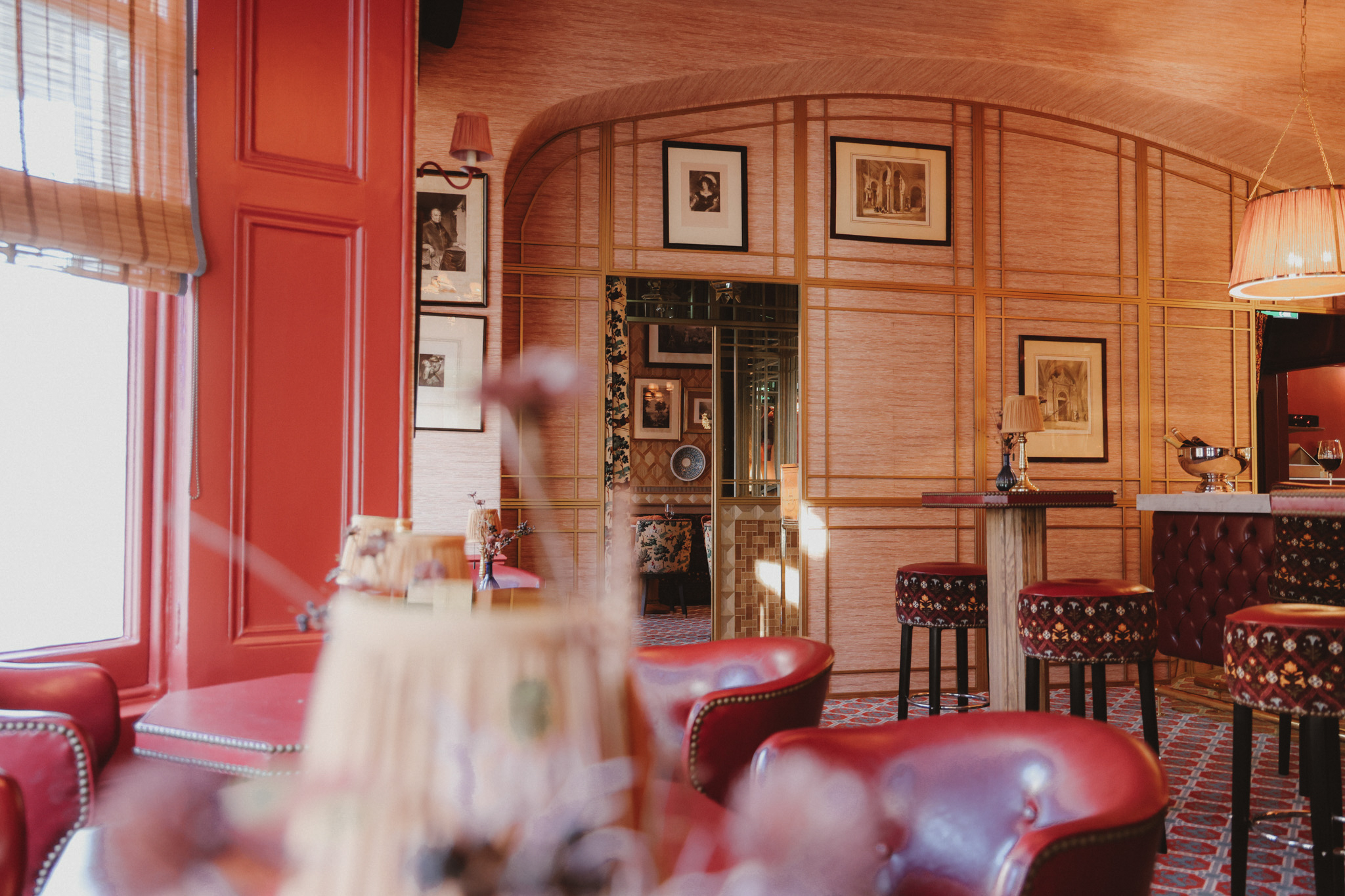 Elegant red bar lounge with leather armchairs, patterned stools, and framed art decor.