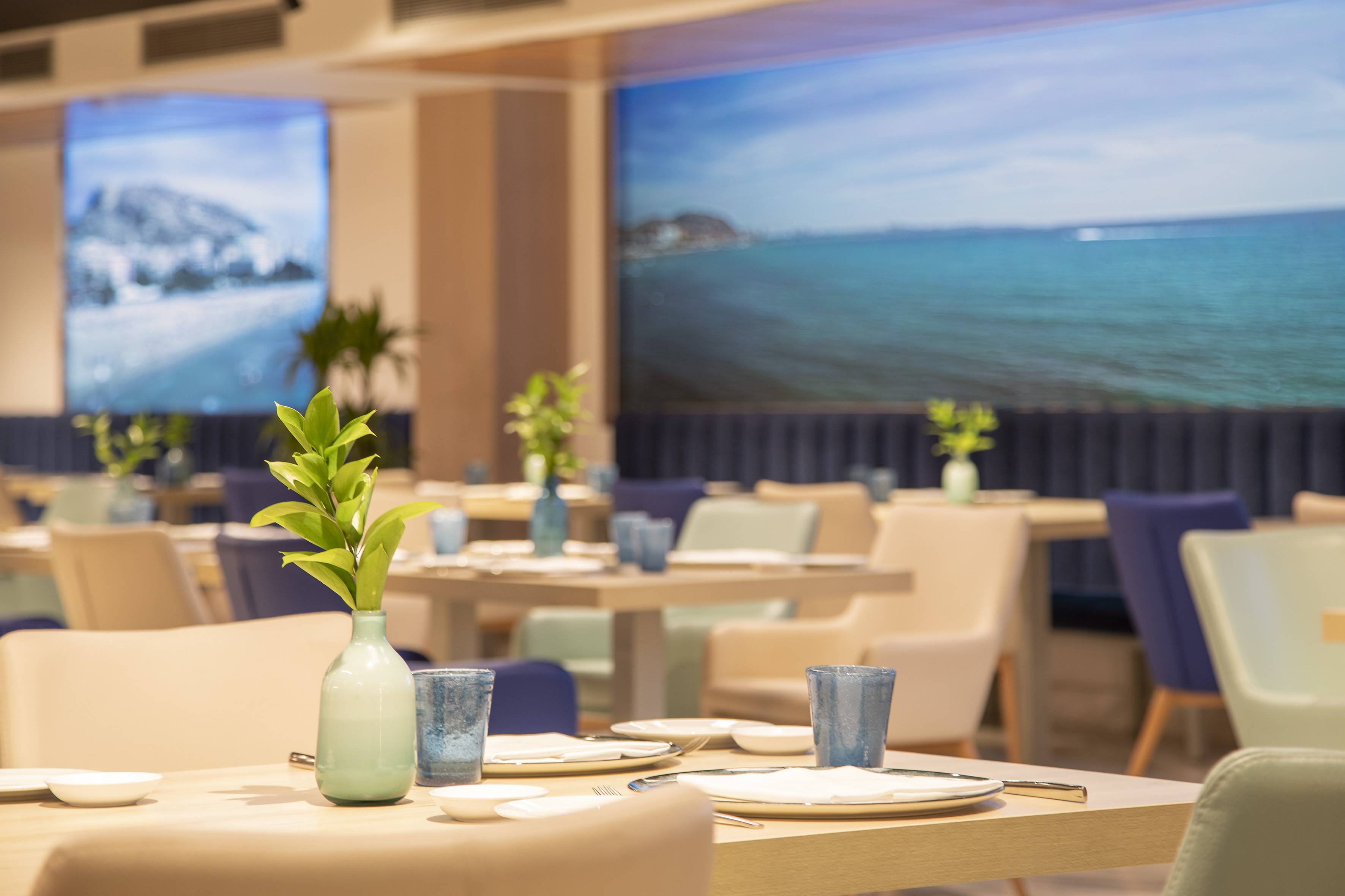 Modern restaurant interior with set tables, plants, and scenic video walls.