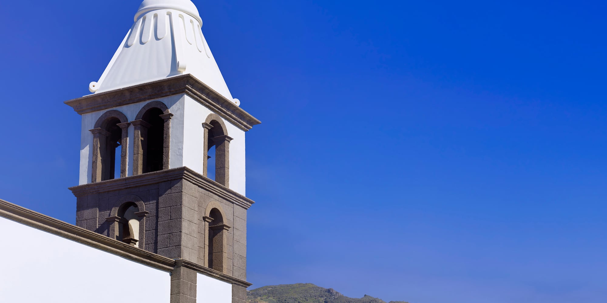 a white tower with a steeple and mountains in the background