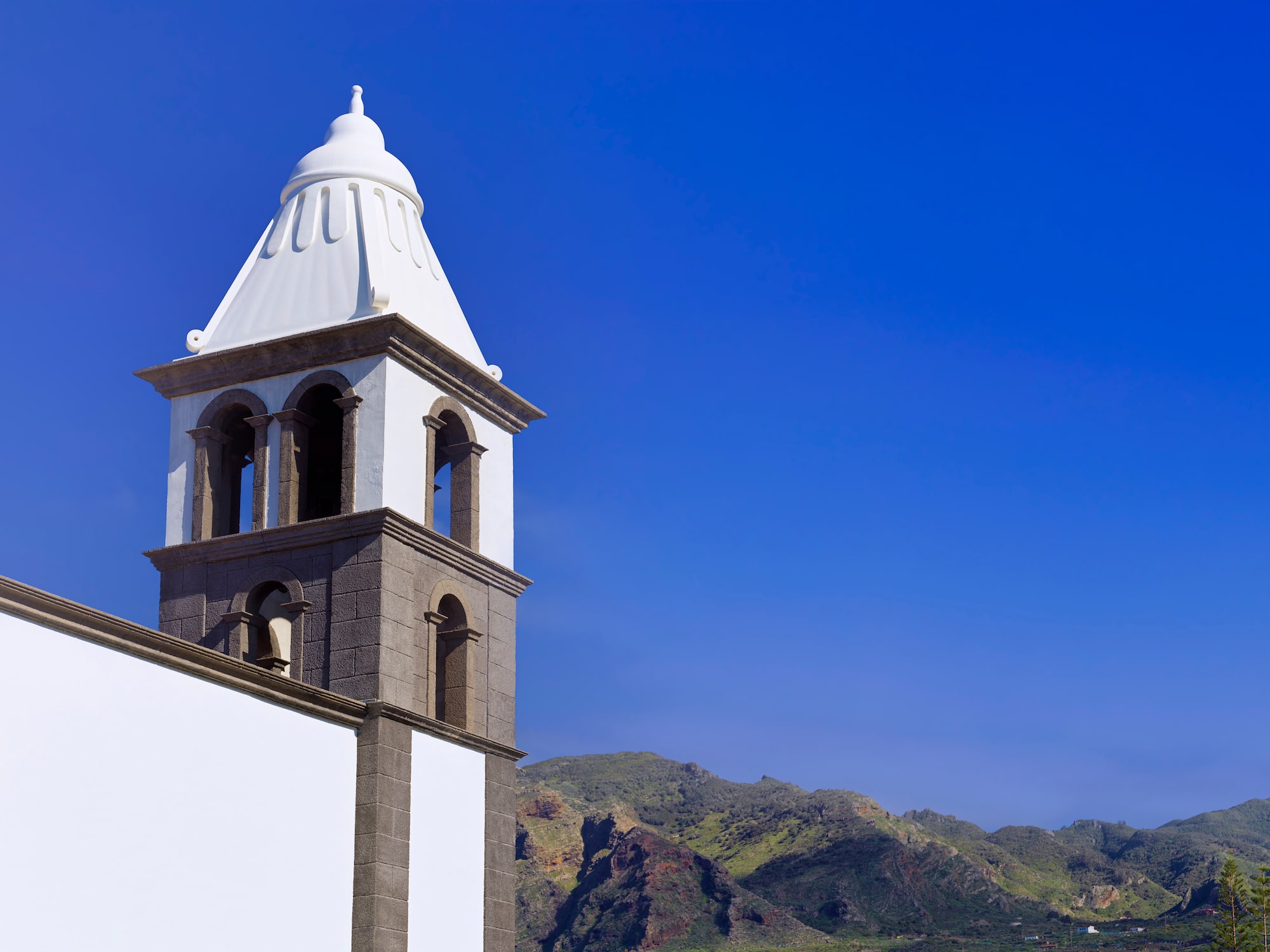 a white tower with a steeple and mountains in the background