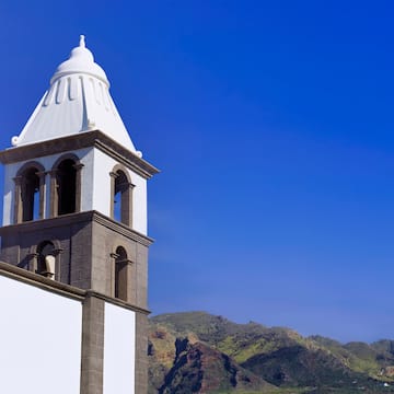 a white tower with a steeple and mountains in the background