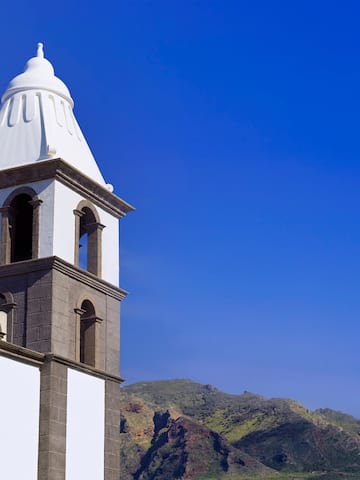 a white tower with a steeple and mountains in the background