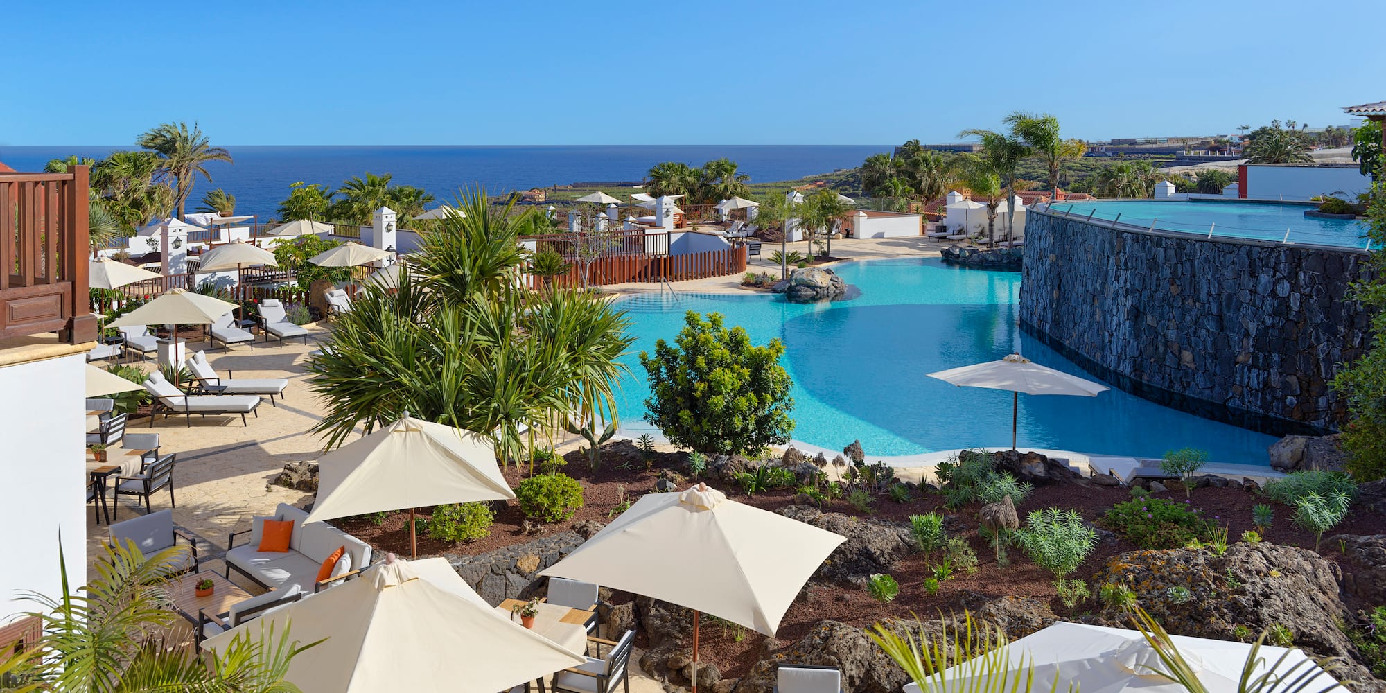 a pool with umbrellas and chairs and a stone wall