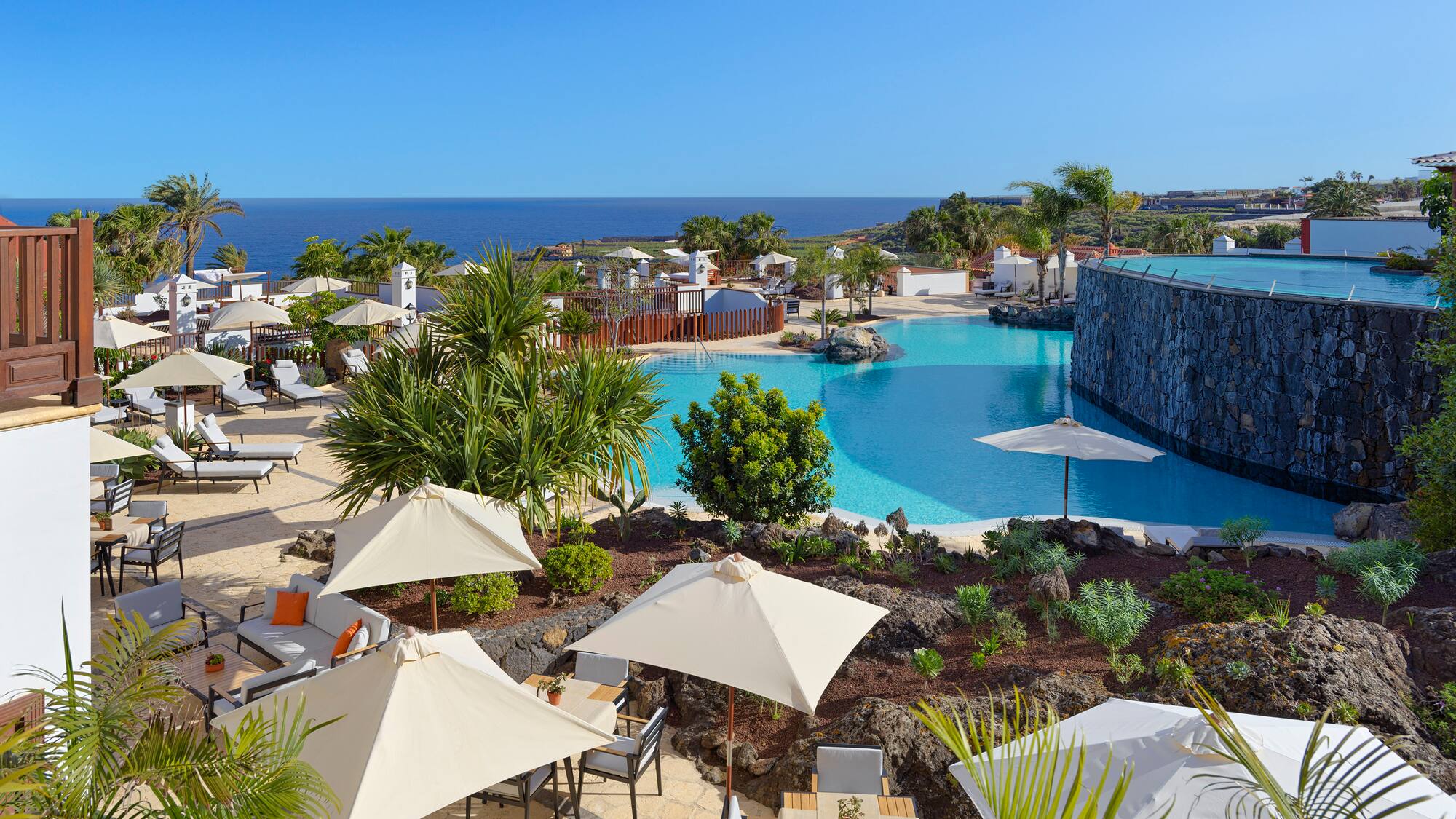 a pool with umbrellas and chairs and a stone wall