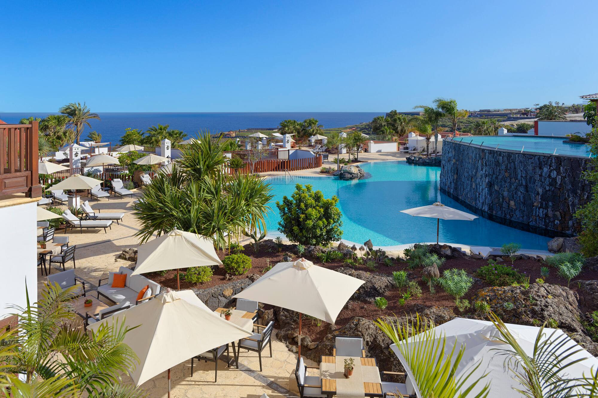 Luxury resort pool with ocean view, palm trees, and outdoor seating areas.