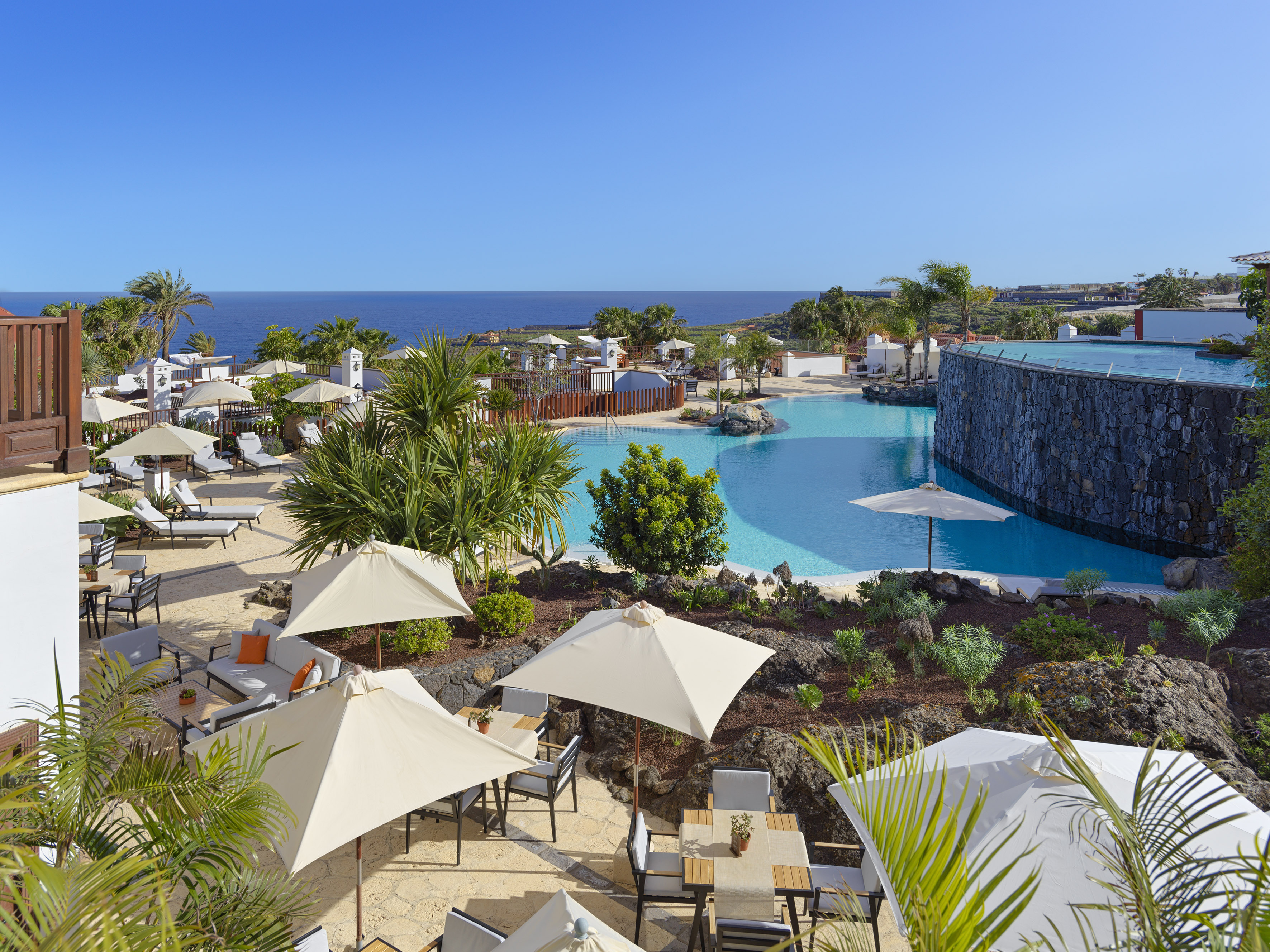 Luxury resort pool with ocean view, palm trees, and outdoor seating areas.