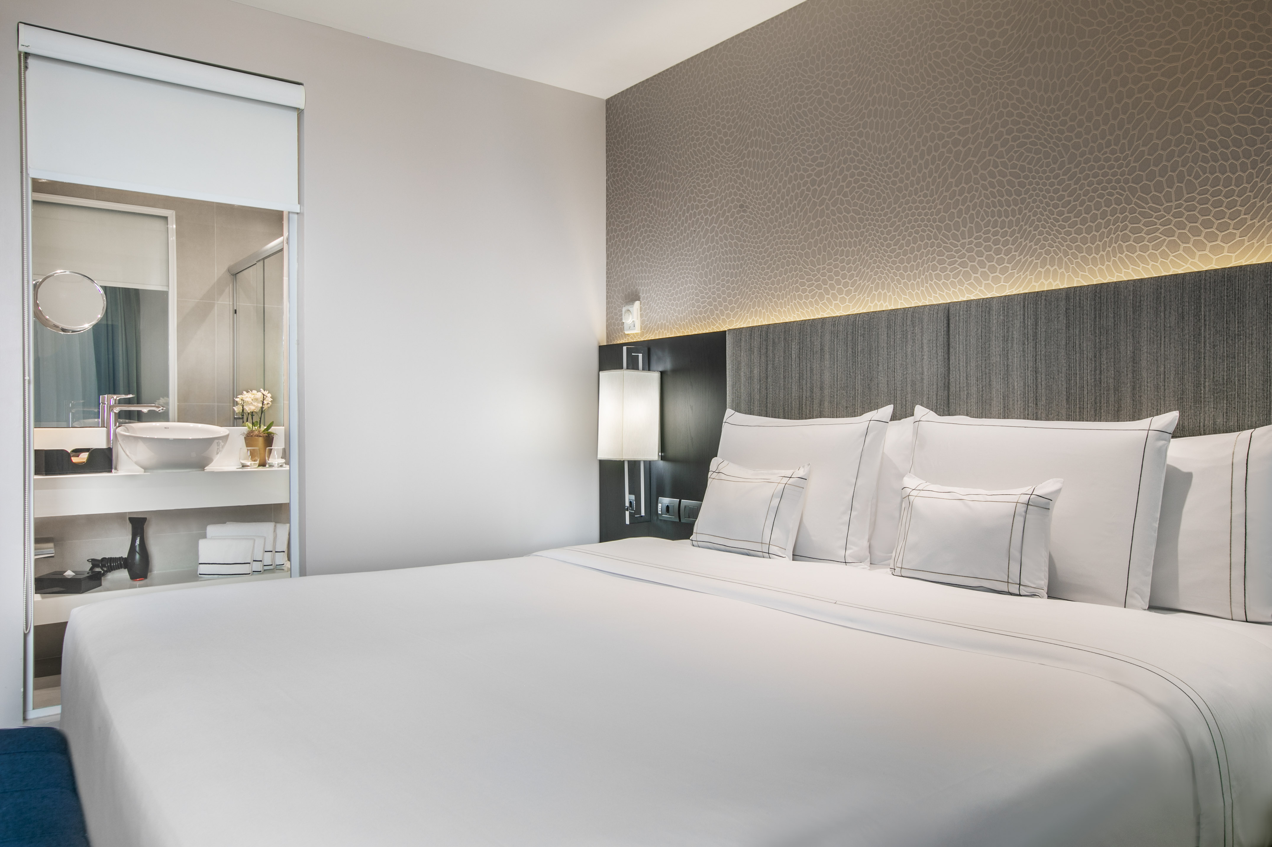 Modern hotel bedroom with white bed, illuminated headboard, and integrated bathroom.