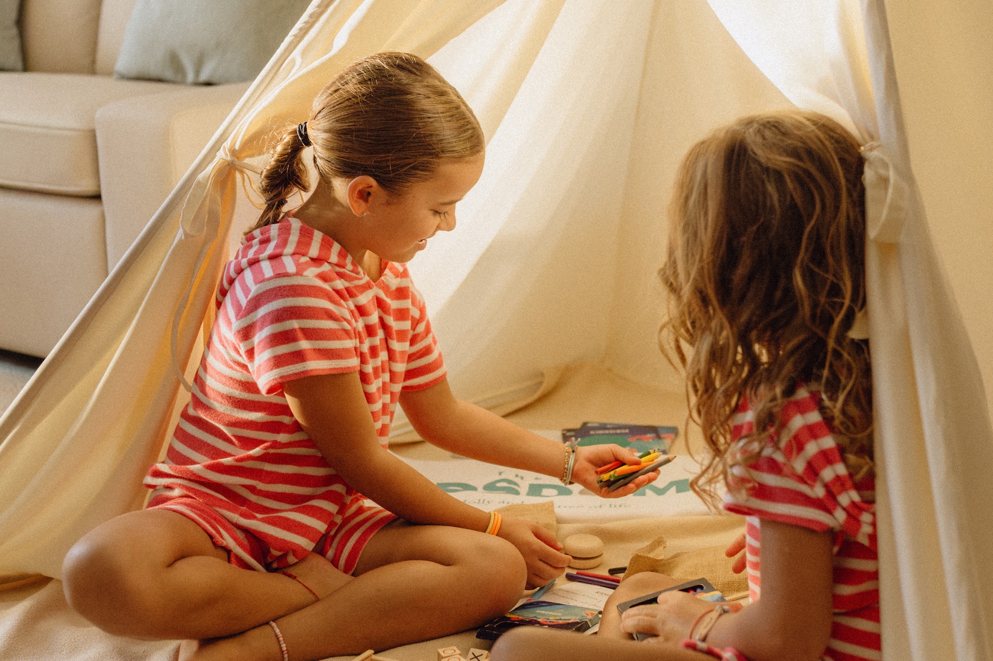 Girls playing with crayons and games inside an indoor teepee tent.