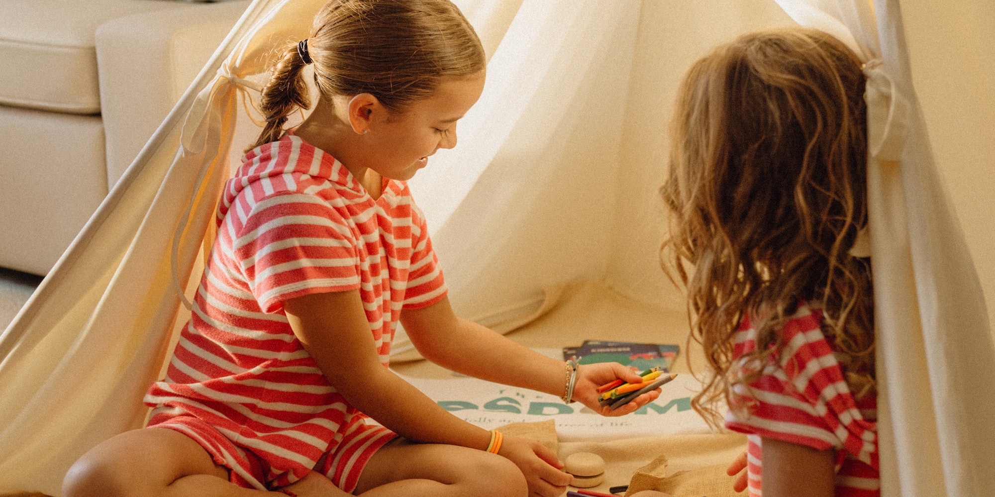 Girls playing with crayons and games inside an indoor teepee tent.