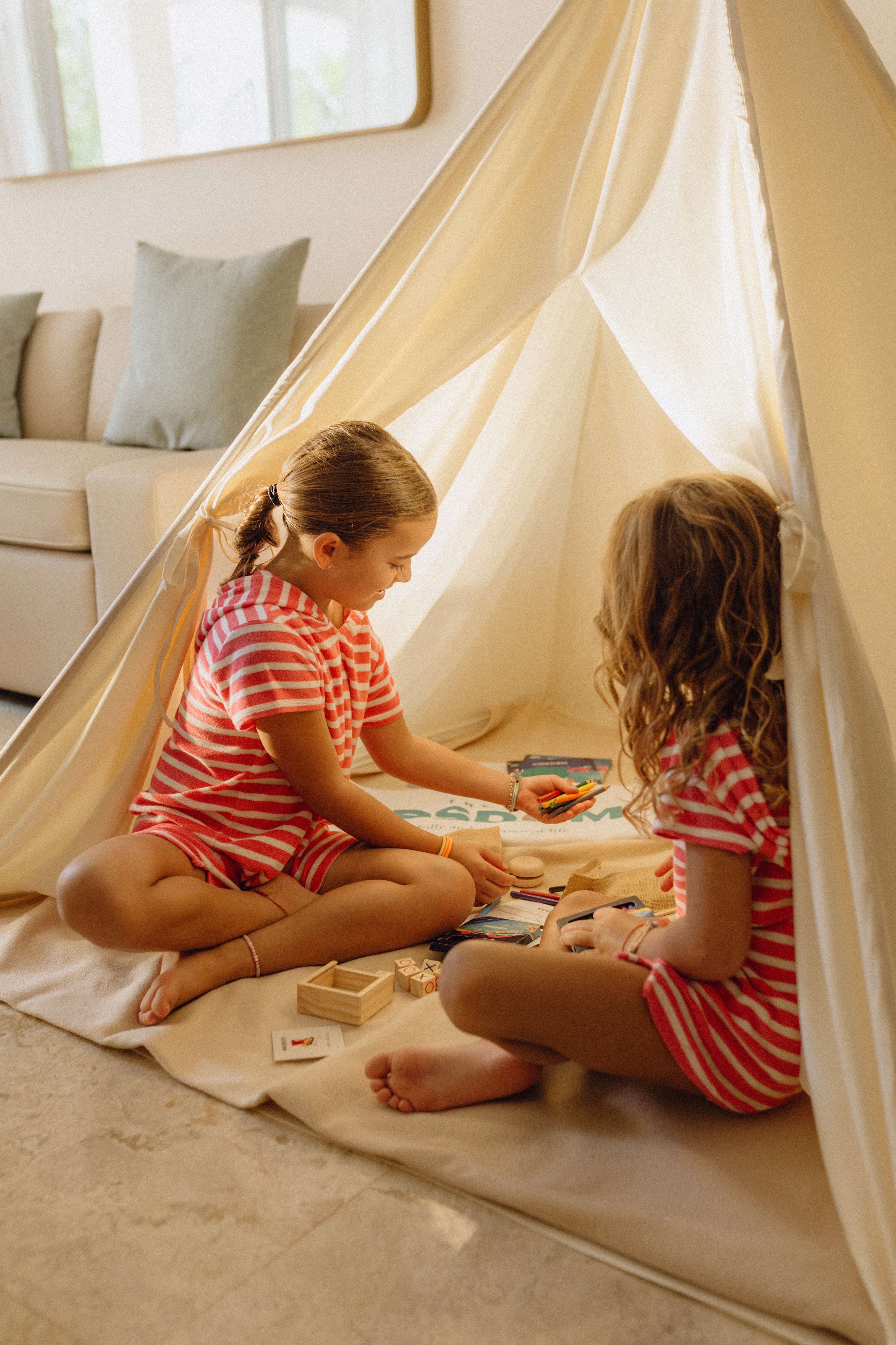 Girls playing with crayons and games inside an indoor teepee tent.