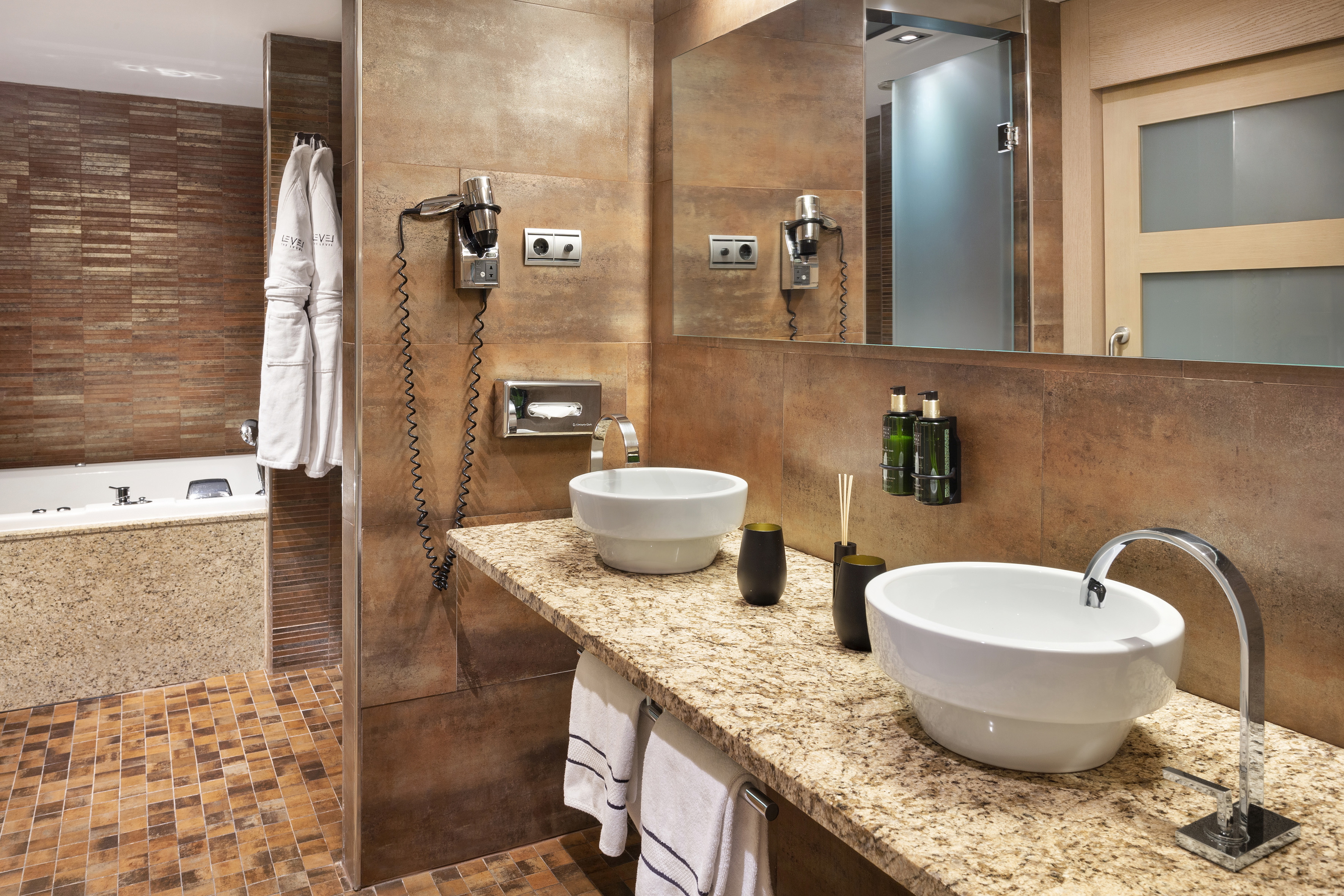 Modern hotel bathroom with double vanity, granite counter, and tiled walls.