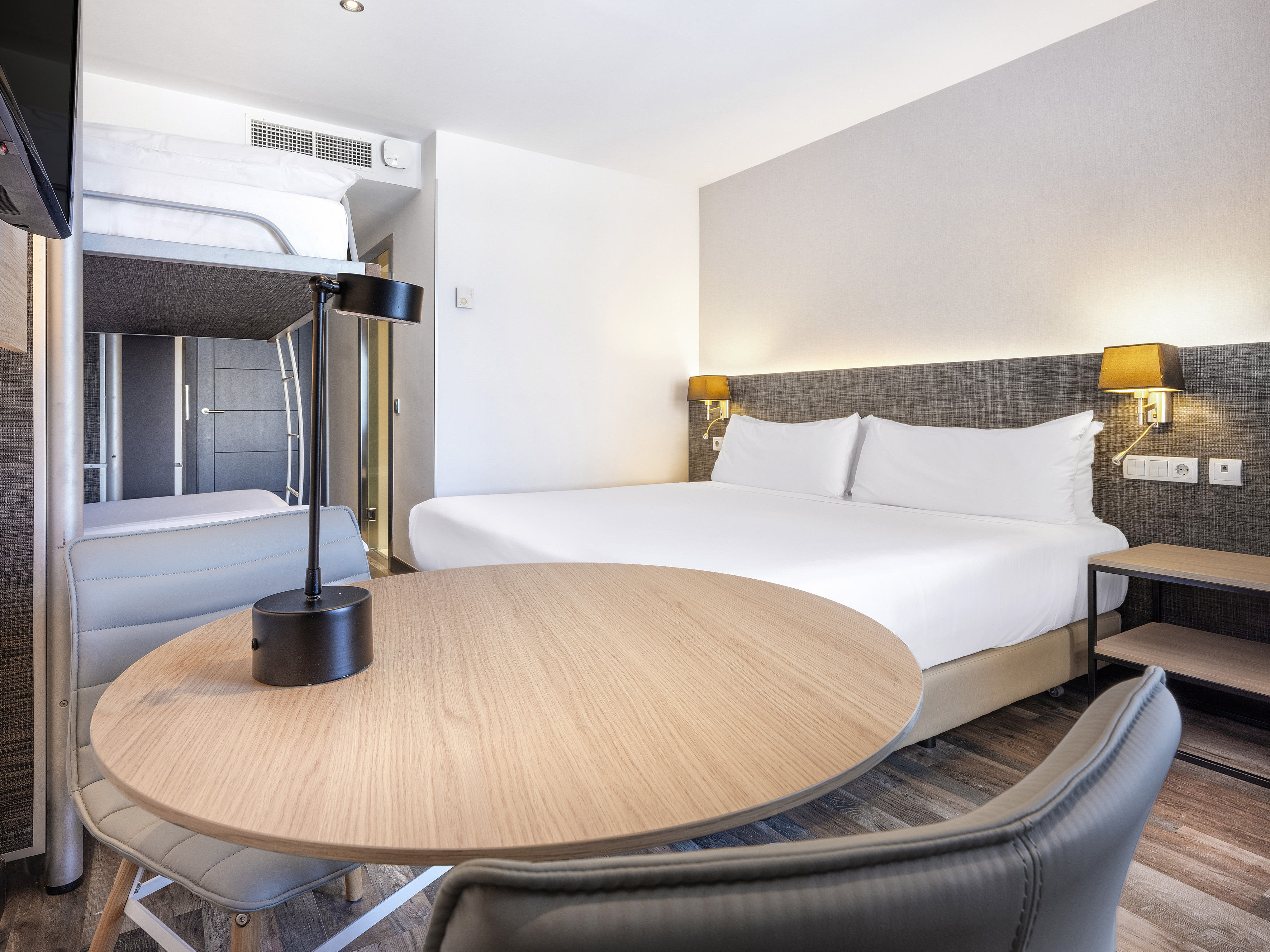 Hotel family room with a comfortable double bed, bunk bed, and table.