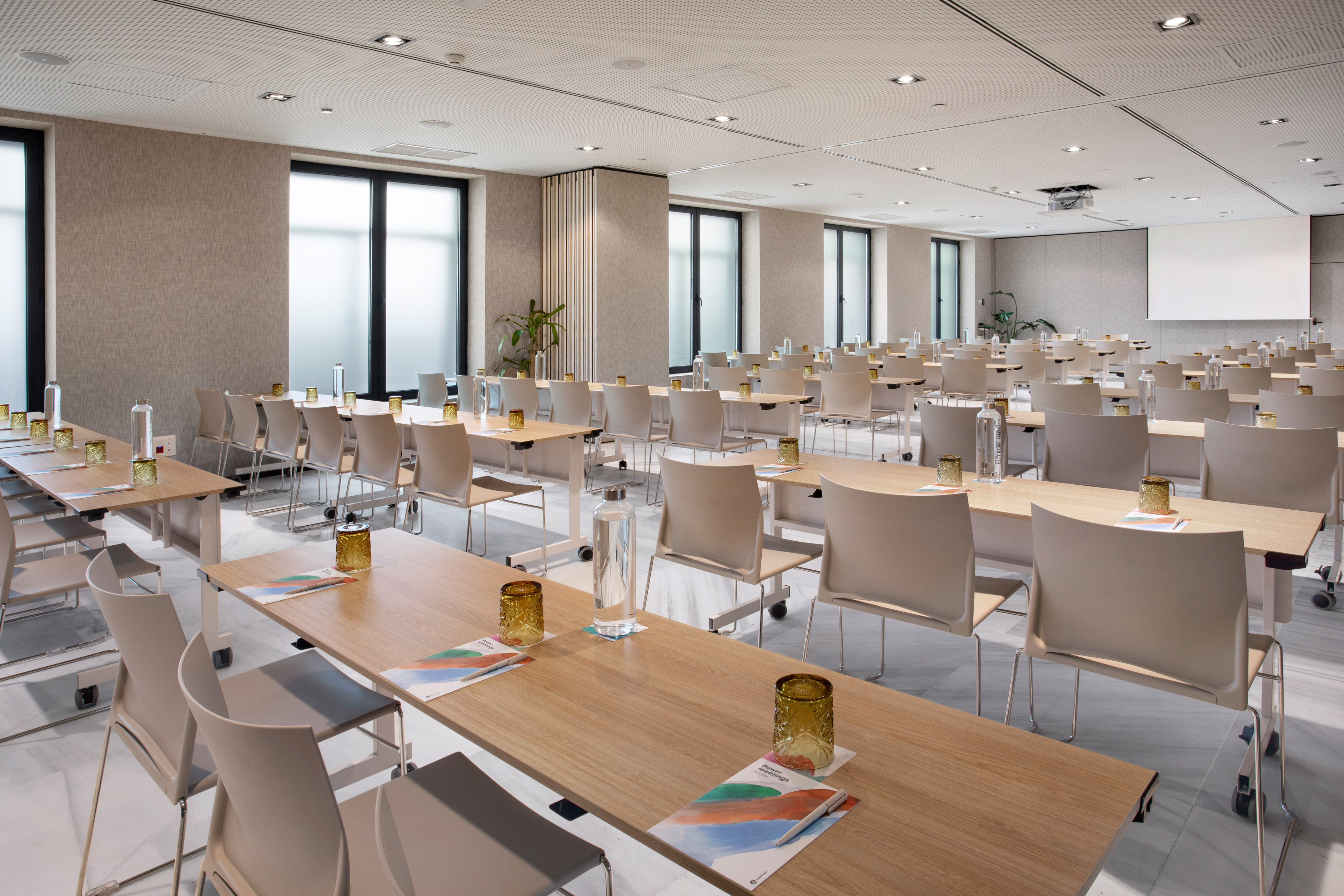 Spacious modern conference room with rows of tables, chairs, projector, and screen.