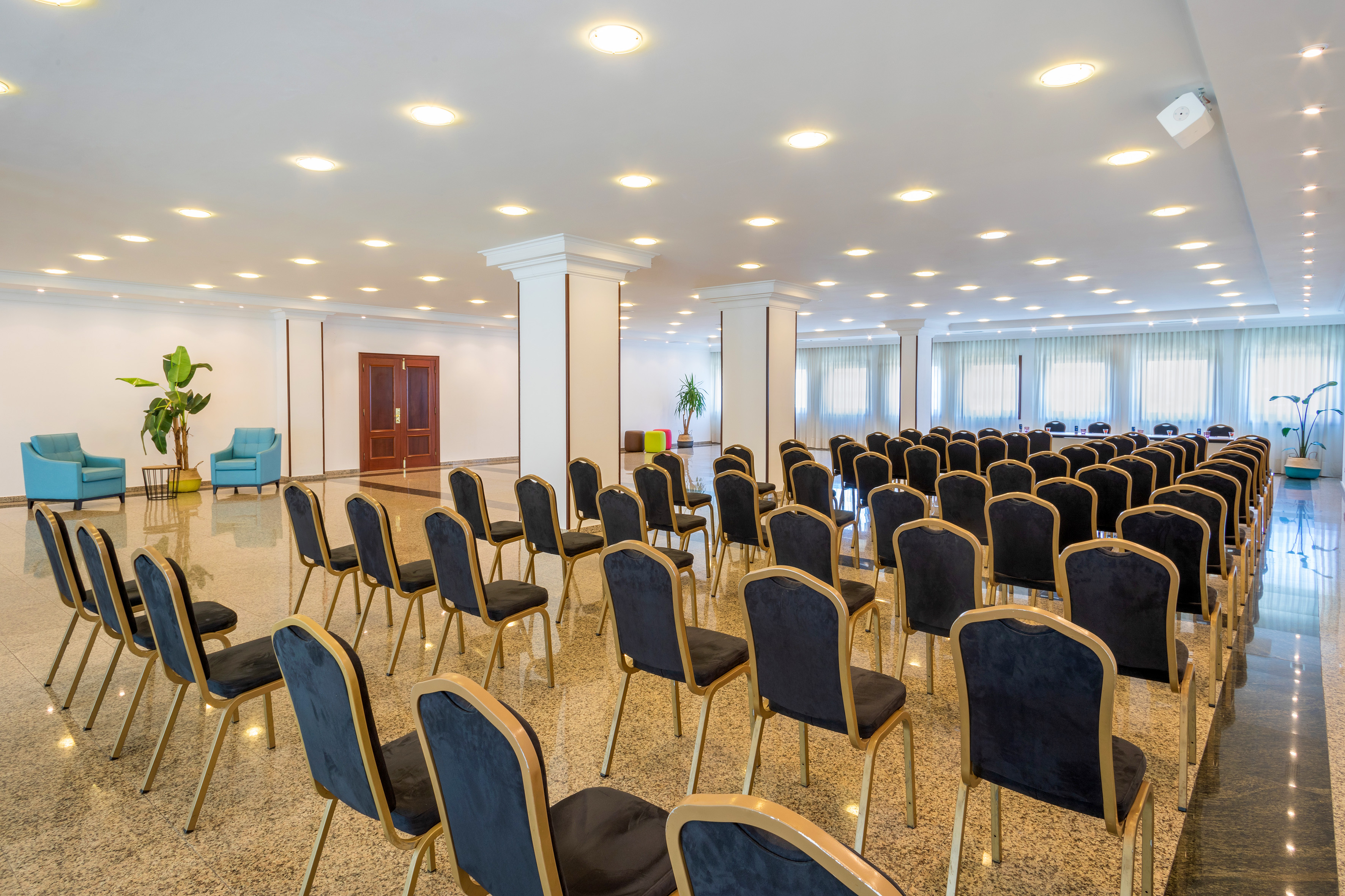 Spacious event venue with rows of black chairs, bright lighting, and a lounge area.