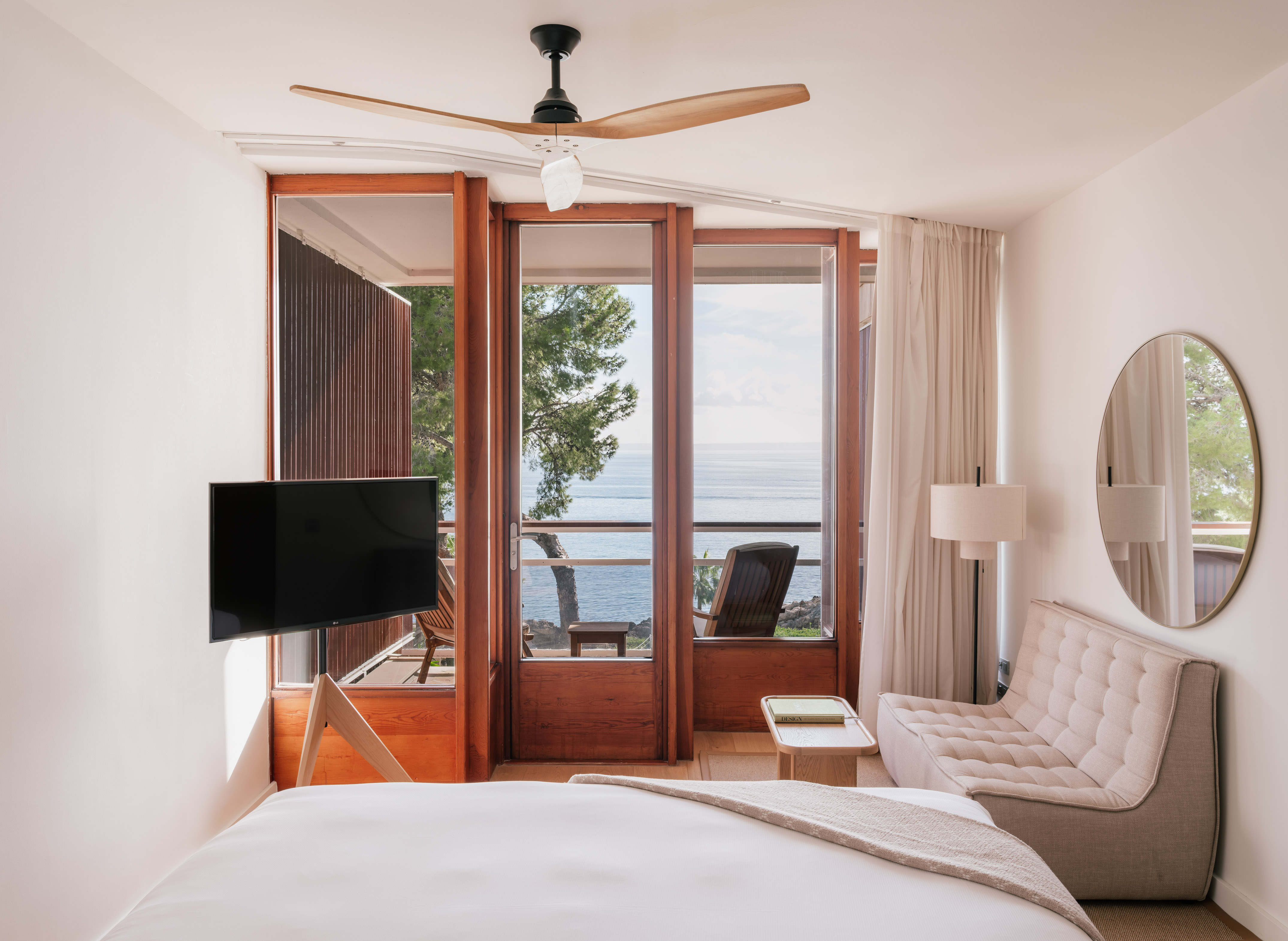 Luxury bedroom with sea view balcony, white bed, modern TV, wooden fan.