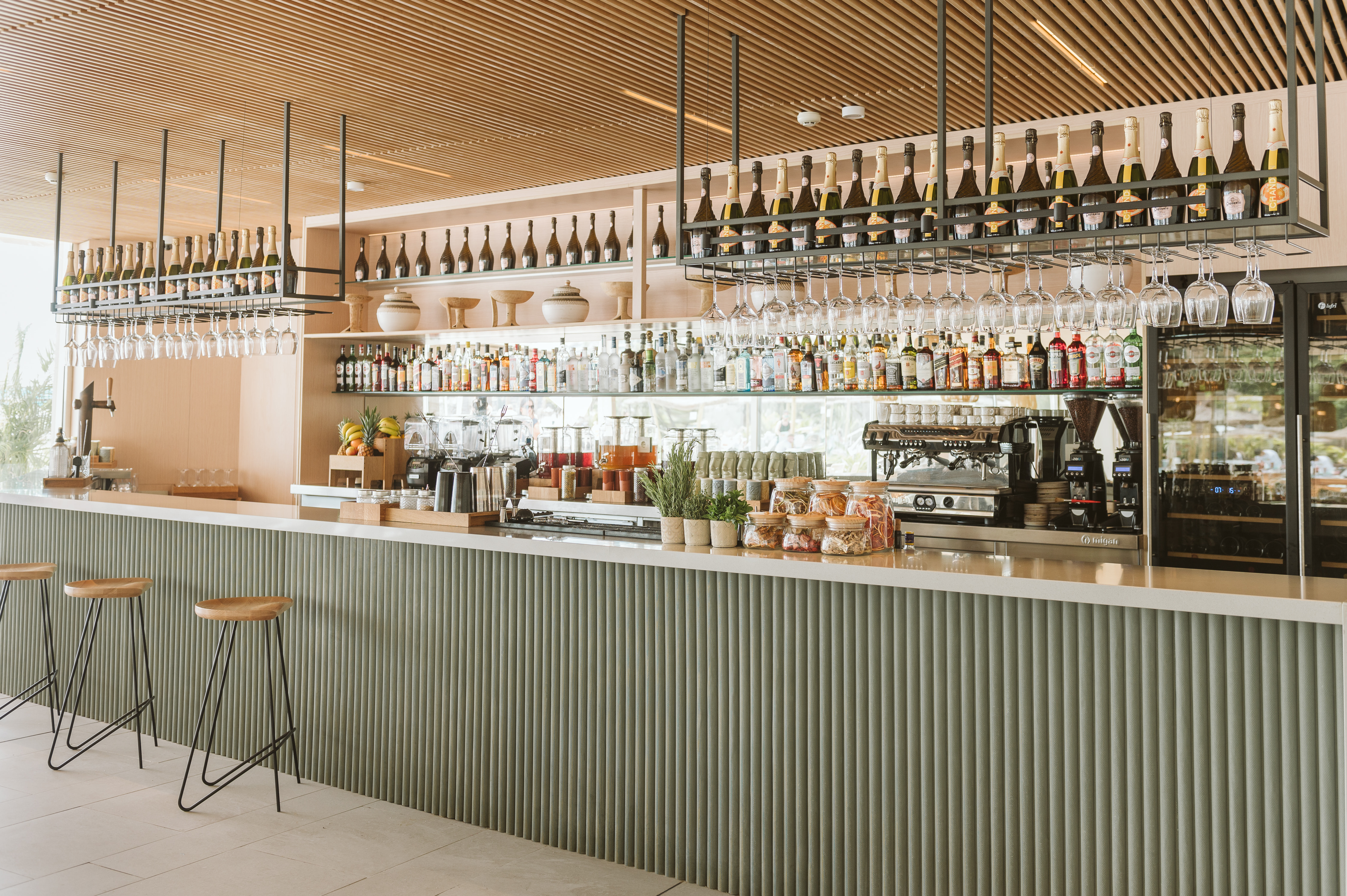 Contemporary bar interior with fluted counter, bottles, glasses, and stools.