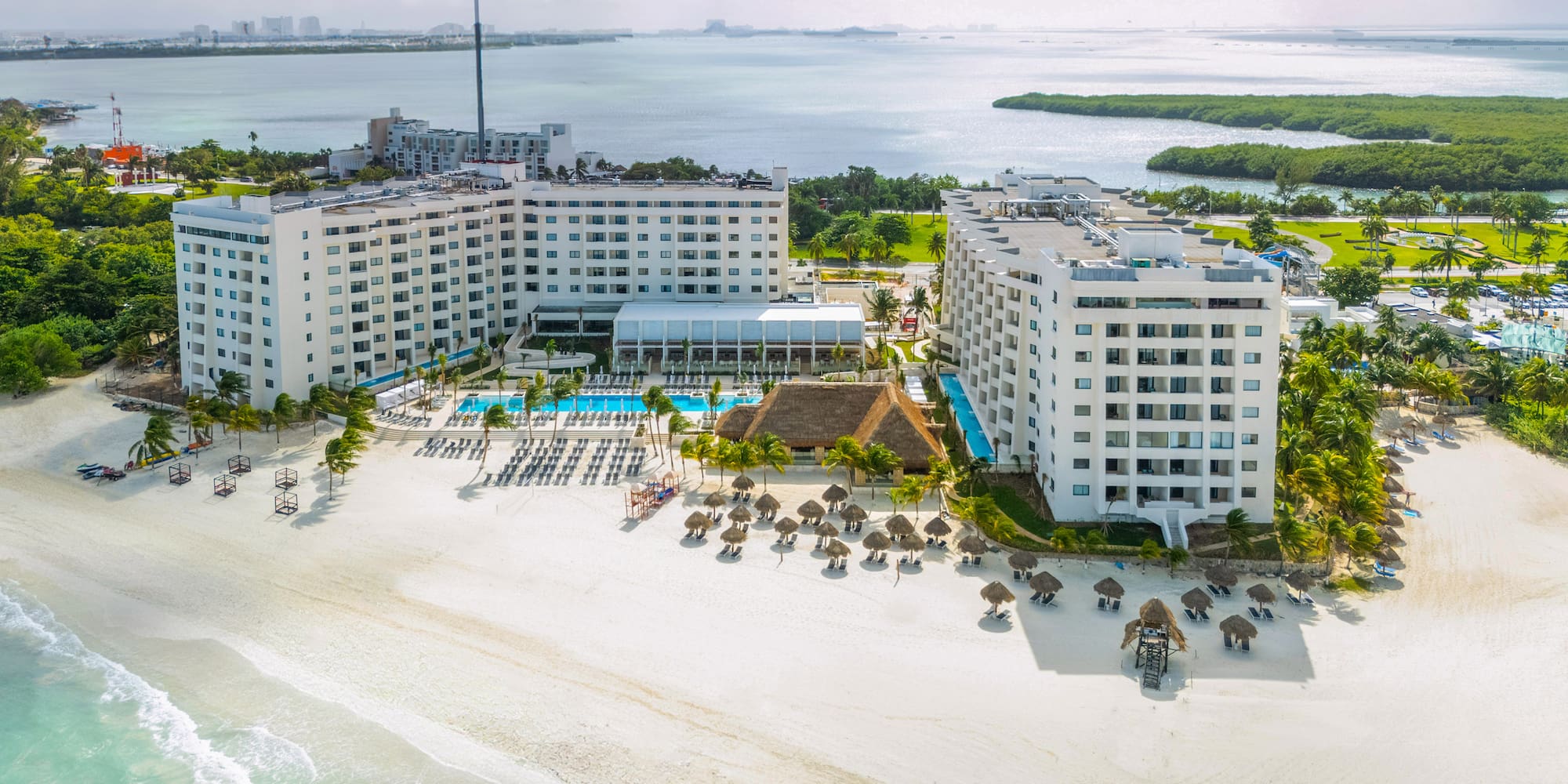 a large white building with a pool and umbrellas on a beach