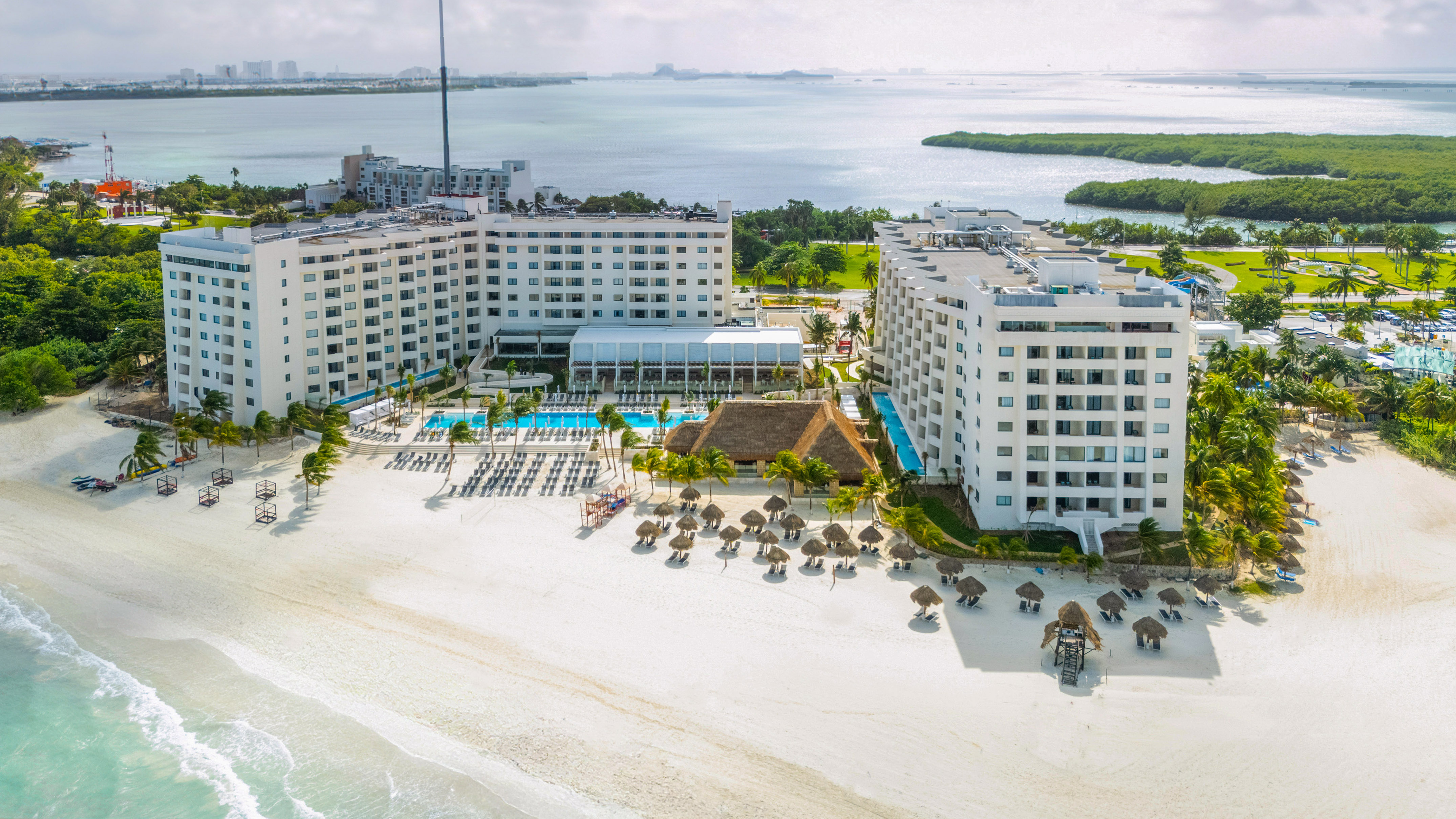 a large white building with a pool and umbrellas on a beach