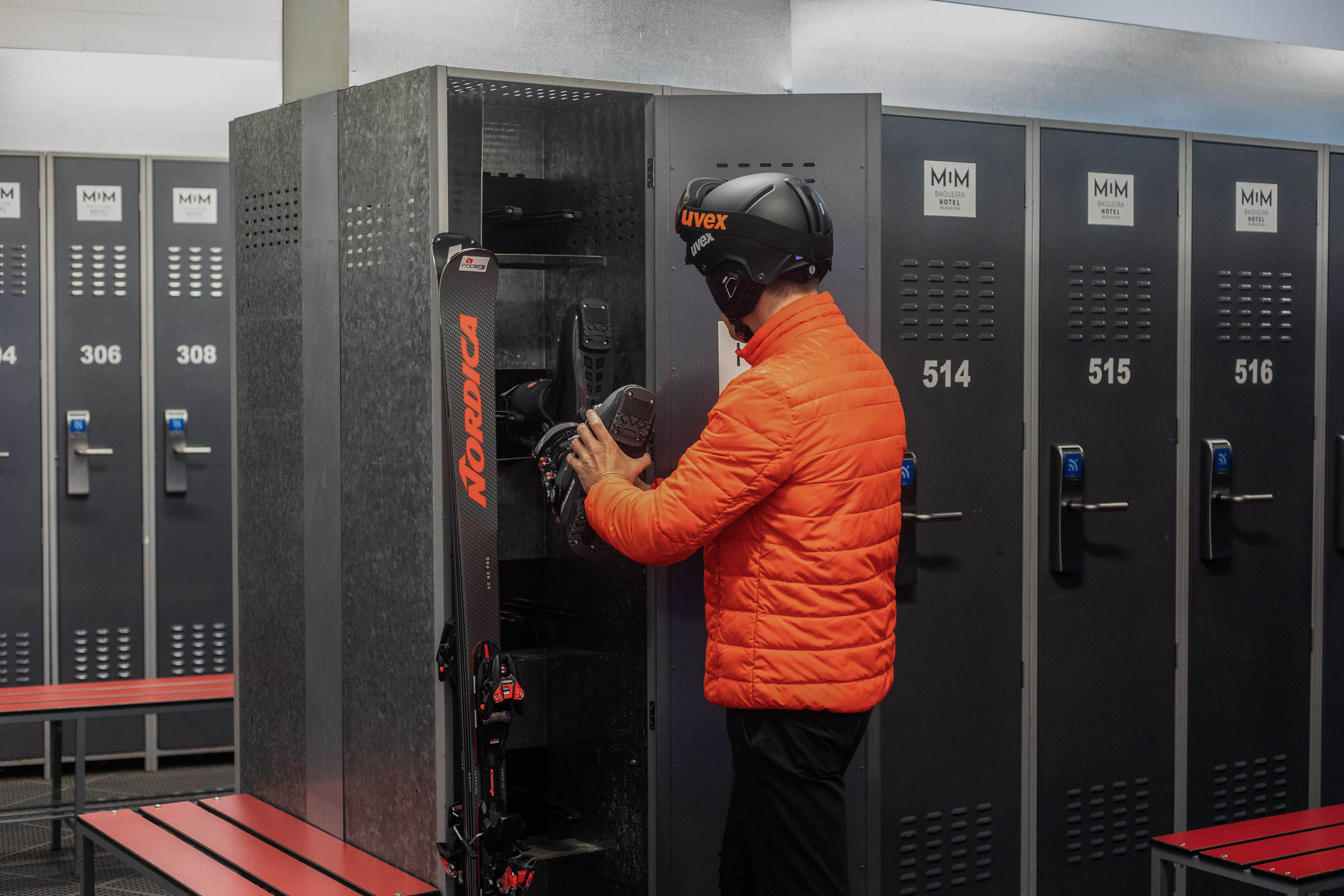Skier storing boots in a MIM Hotel ski locker, with Nordica skis nearby.
