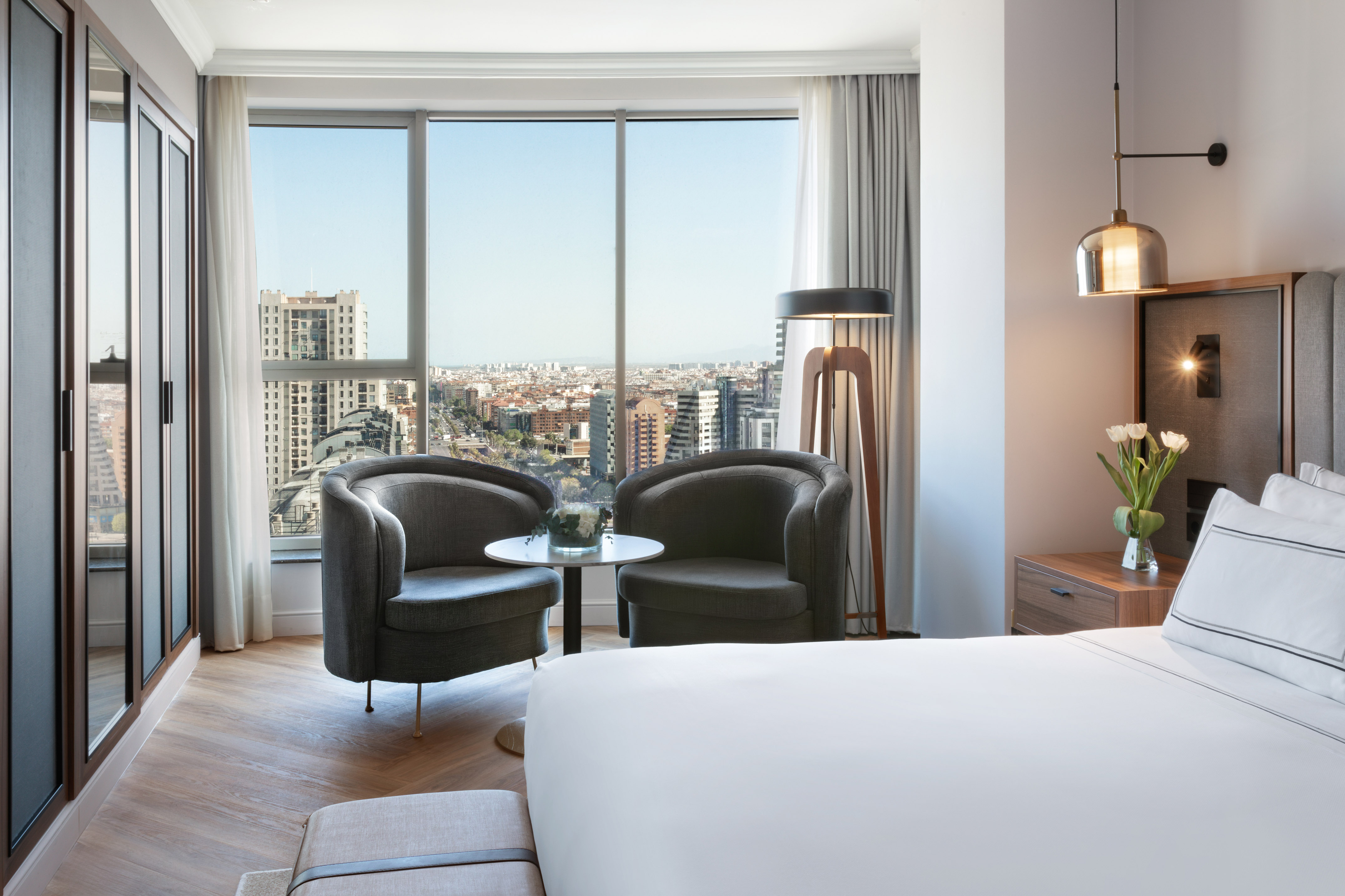 Lujosa habitación de hotel con vista a la ciudad, cama y sillones.