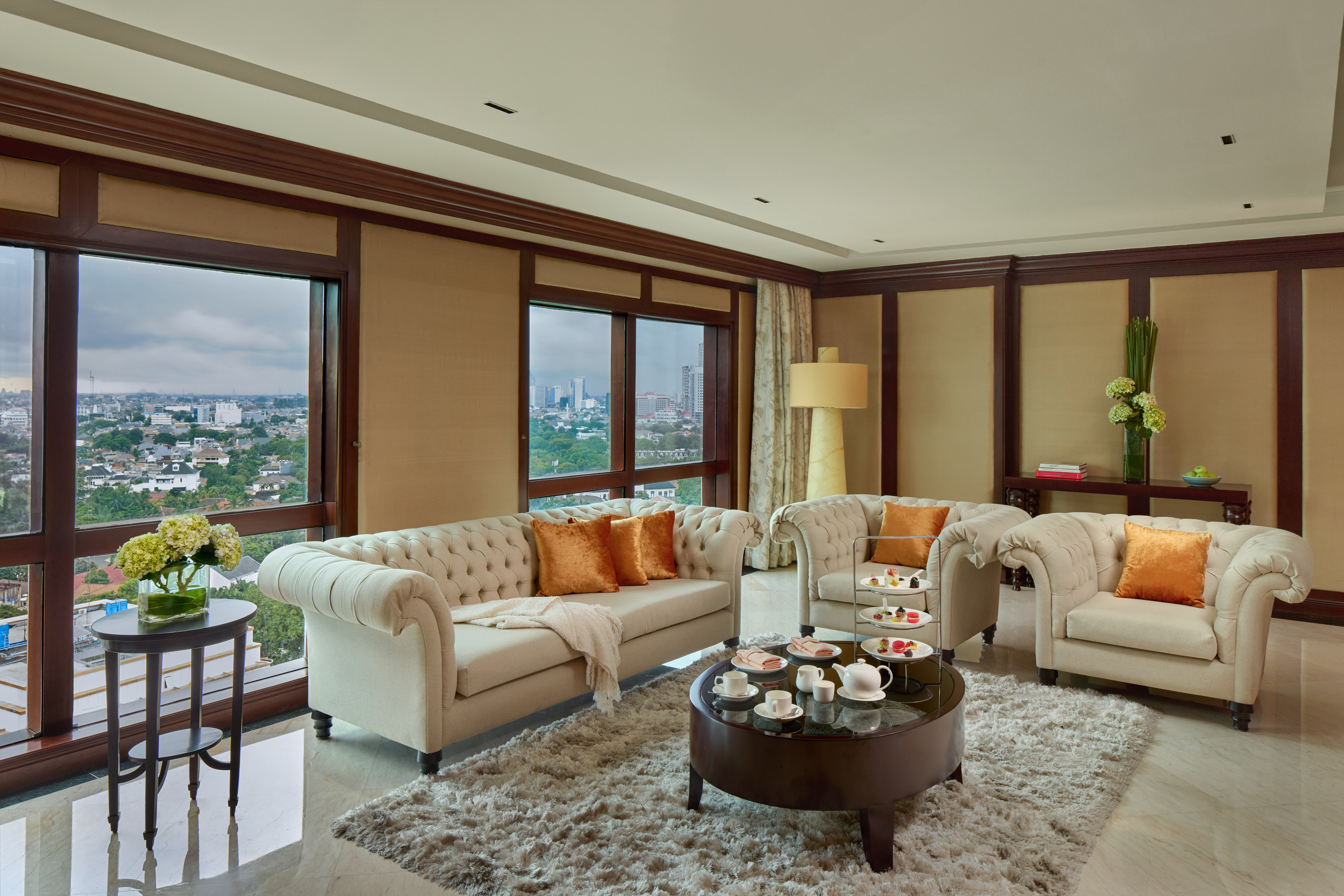 Luxury hotel suite living room with city view, tufted sofas, and tea service.