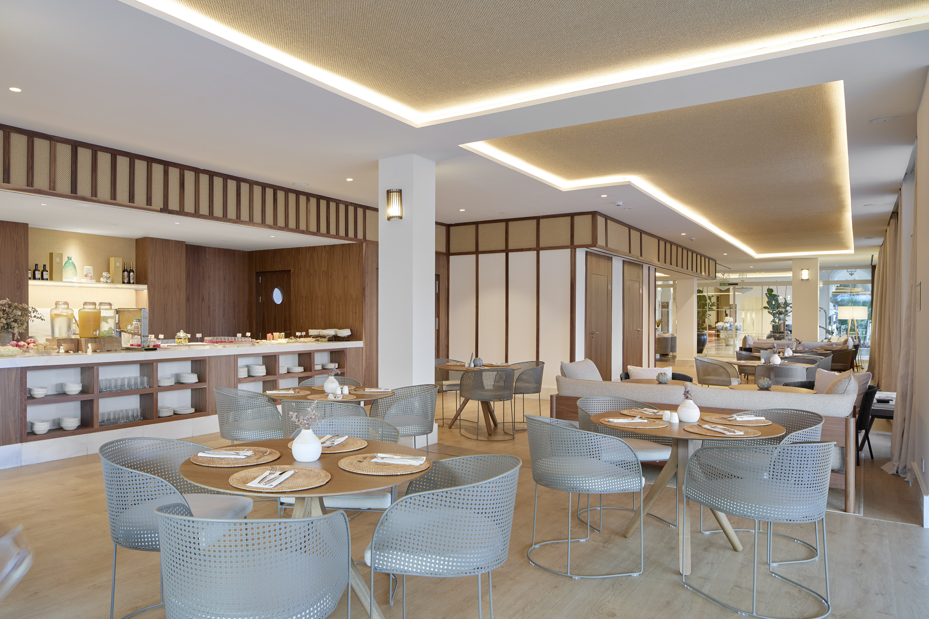 Modern hotel dining room with breakfast buffet and gray chairs.