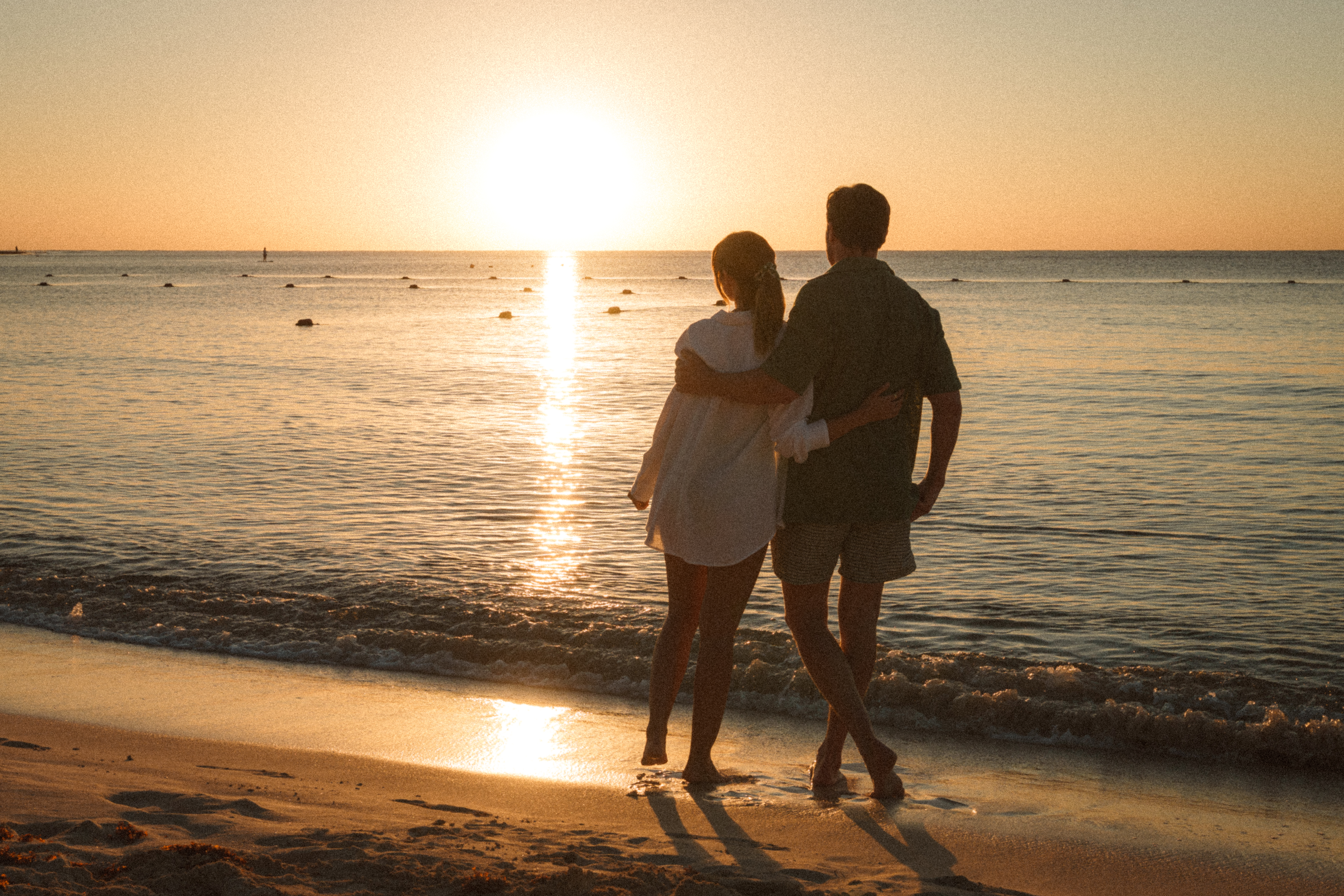 a man and woman standing on a beach looking at the sunset