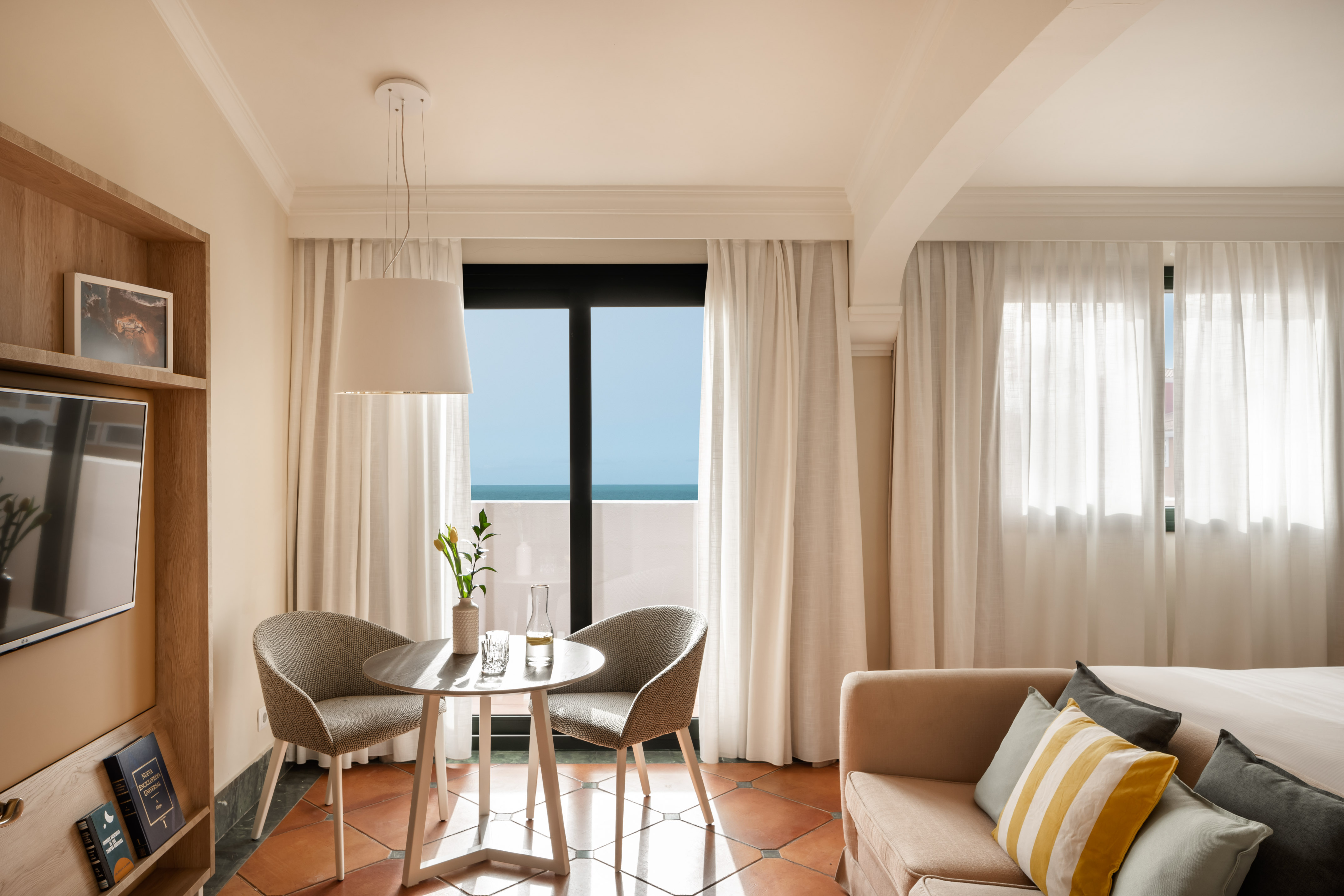 Hotel room with ocean view balcony, modern dining area, and sofa.