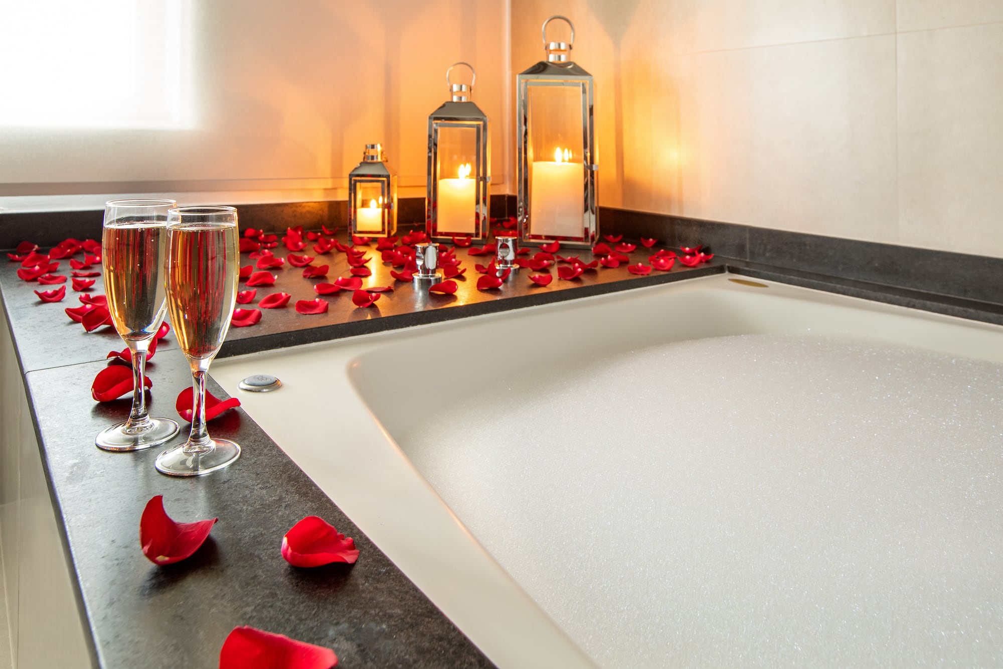Romantic bubble bath with rose petals, champagne, and flickering candles.