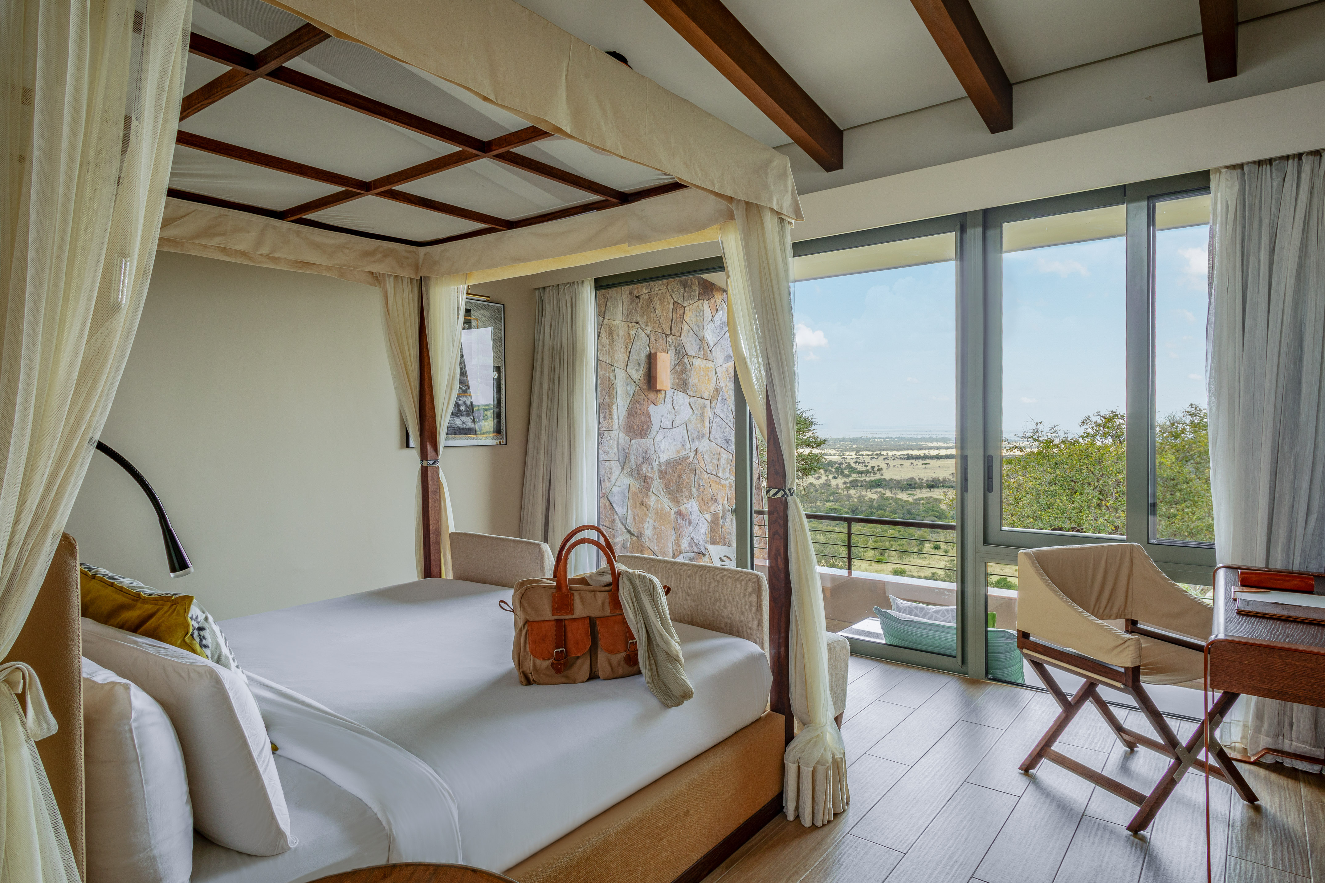 Four-poster bed in a safari lodge bedroom with panoramic savanna views.