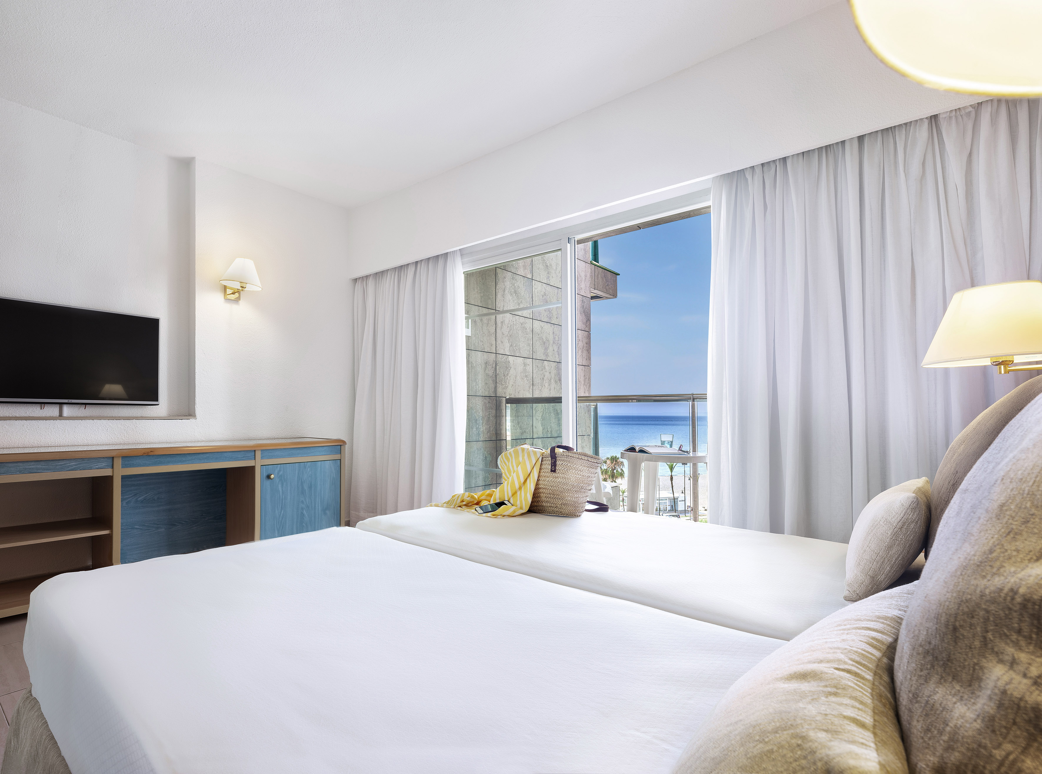 Bright hotel room with twin beds, balcony, and beautiful ocean view.