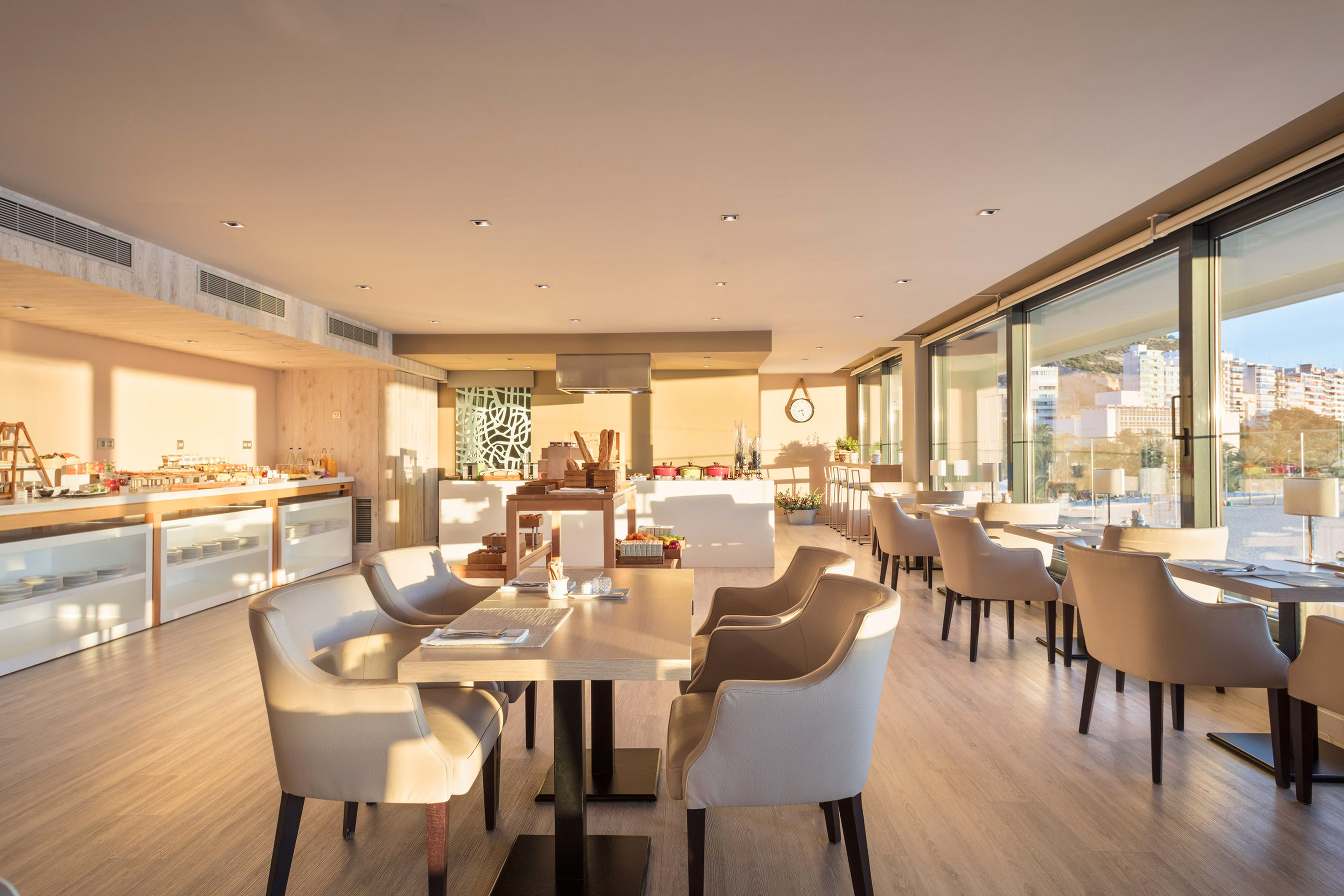 Sunlit hotel breakfast buffet and modern dining area with large windows.