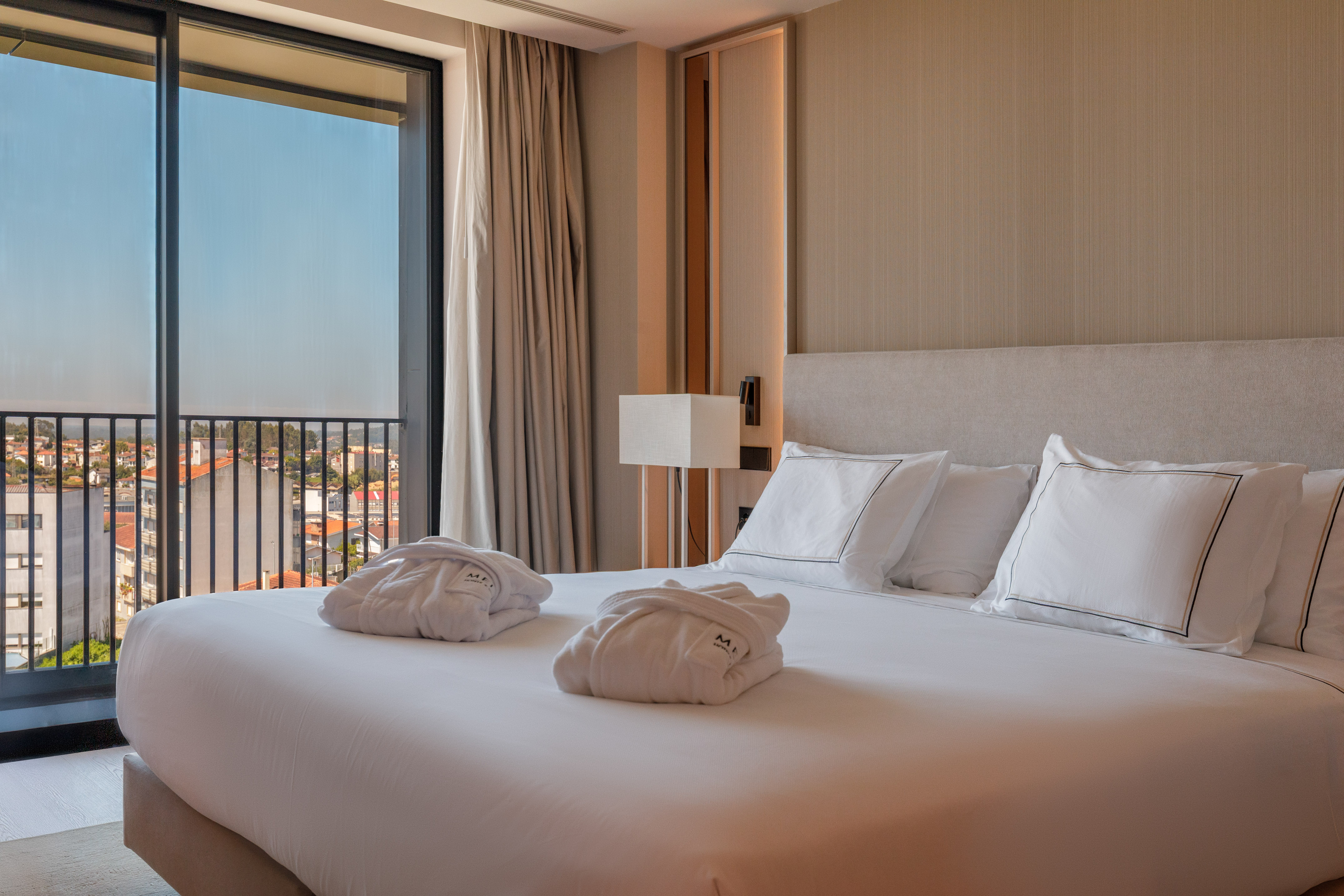 Hotel room with king bed, bathrobes, balcony, and city view.