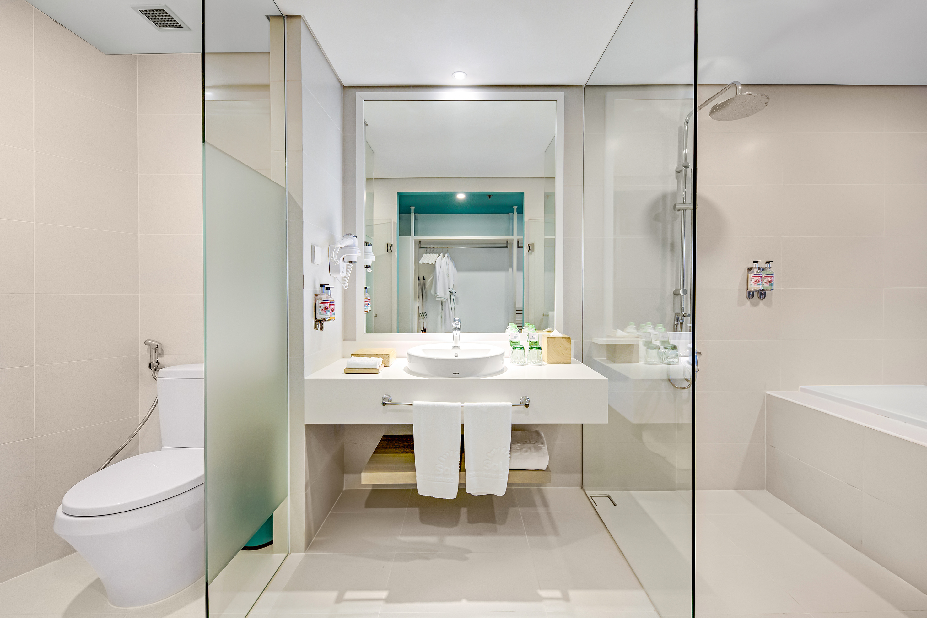 Bright modern hotel bathroom featuring a toilet, vanity, glass shower, and tub.