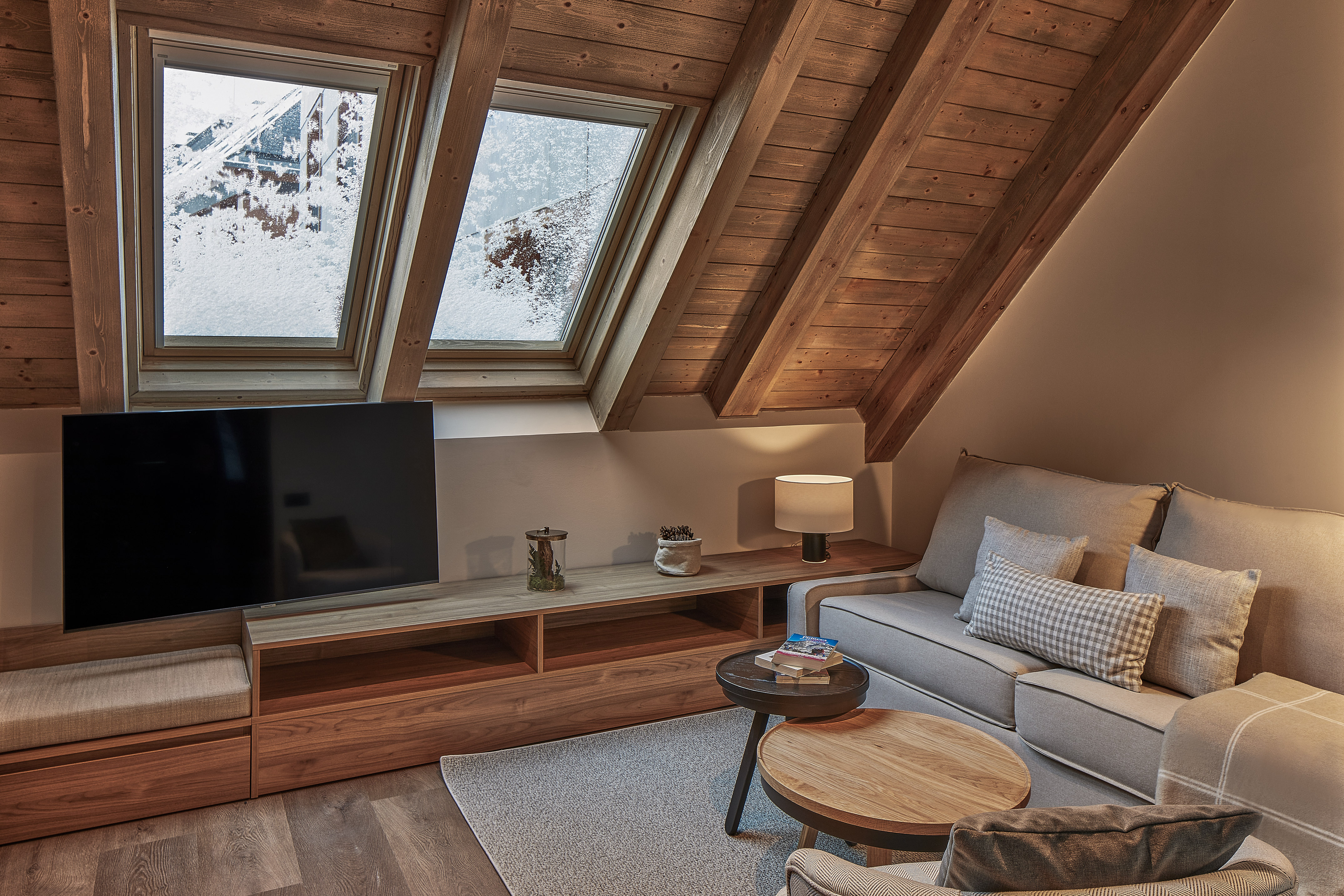 Chalet attic living room with snowy windows, wooden ceiling, sofa, and TV.
