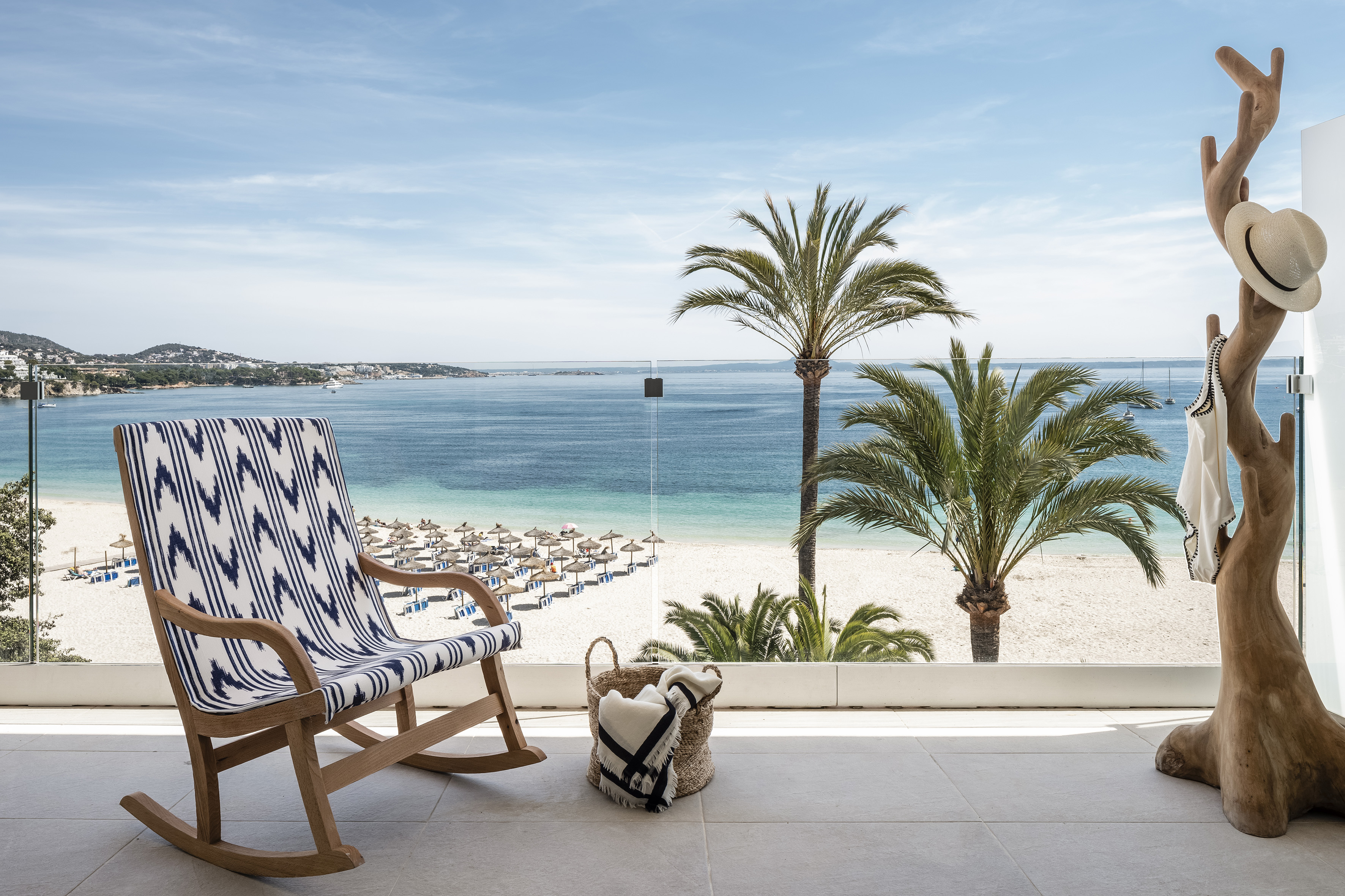 Resort balcony with rocking chair, beach, palm trees, and clear blue sea view.