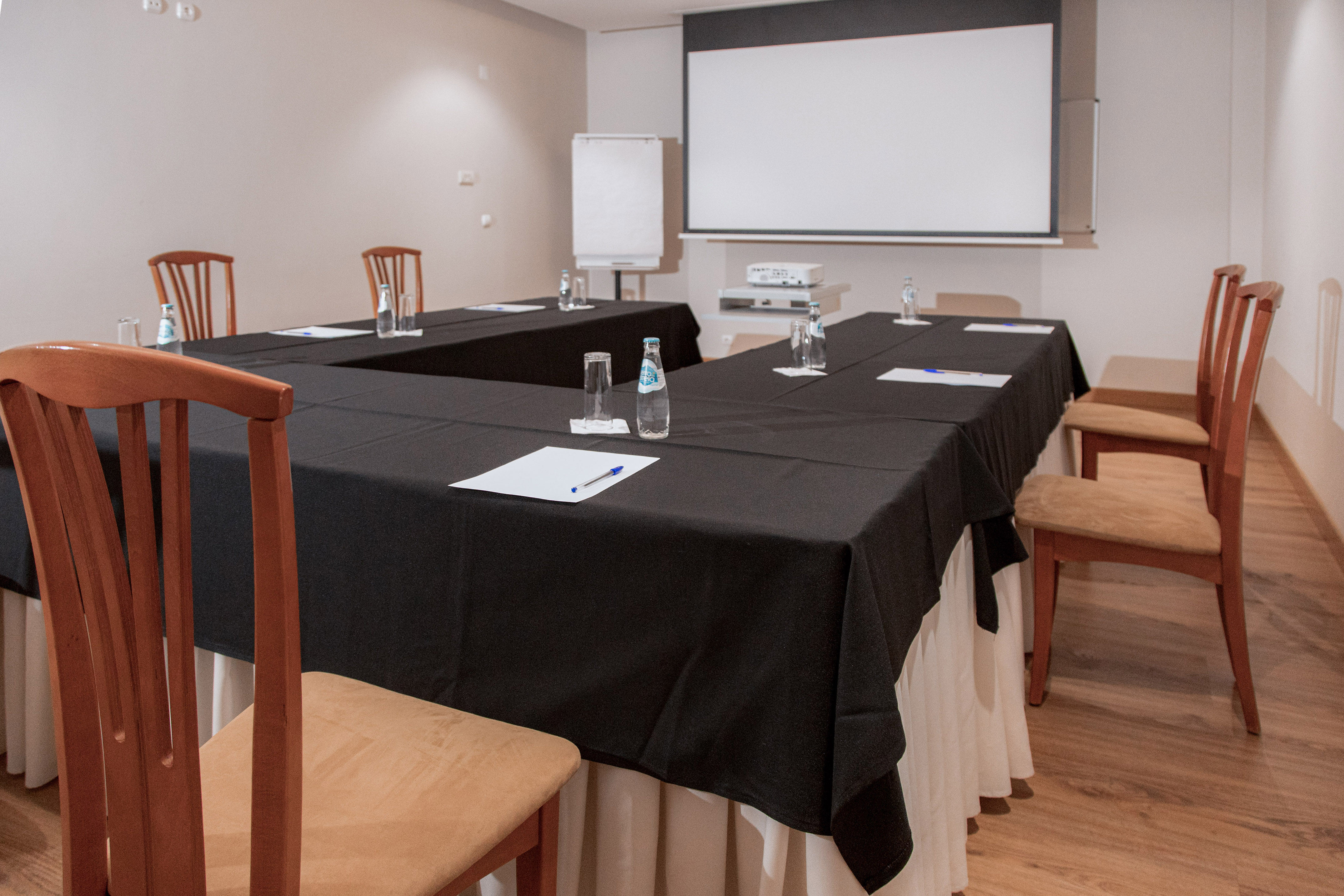 U-shaped meeting room with projector screen, flip chart, and table settings.