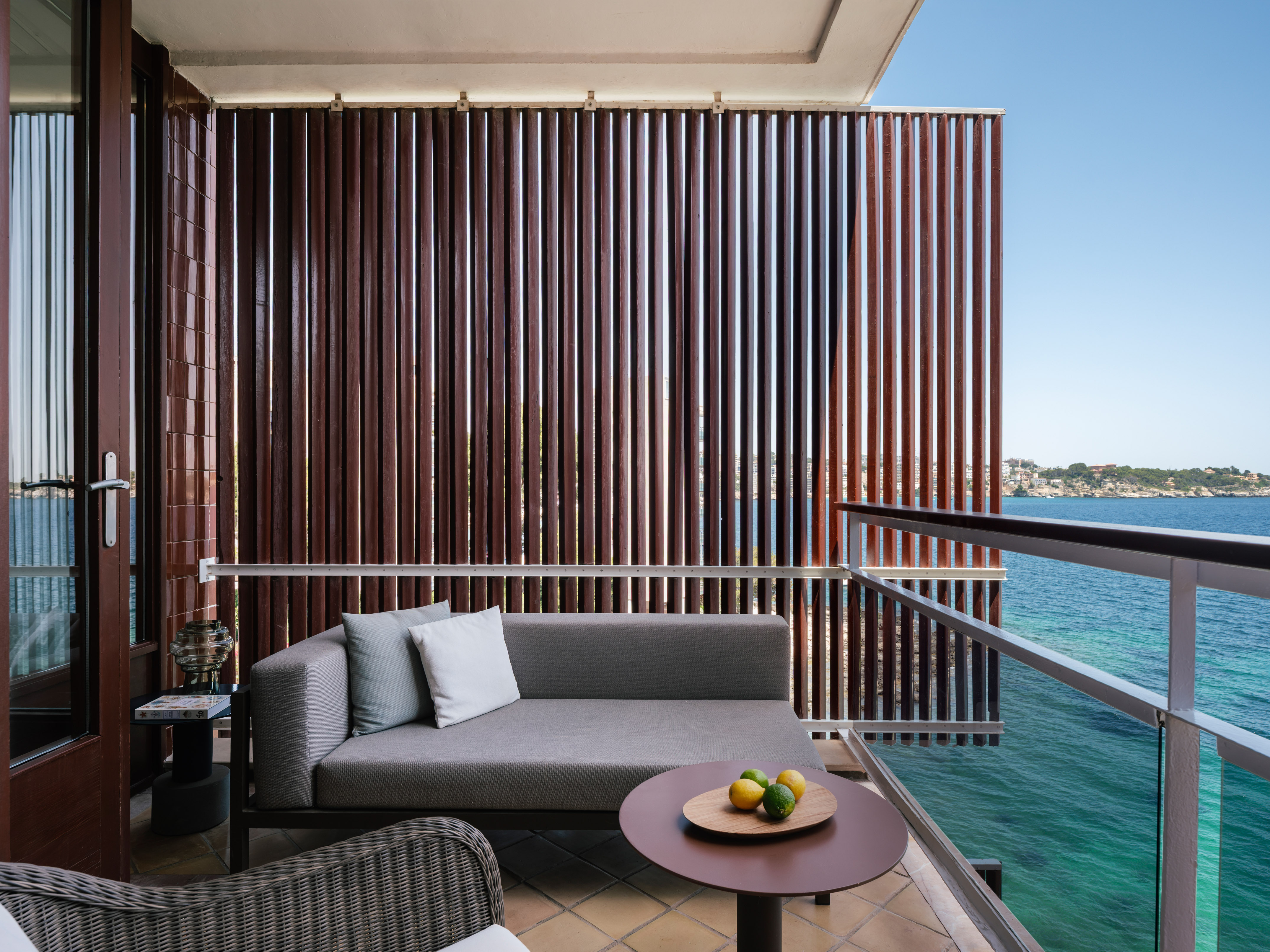 Mediterranean balcony with turquoise sea, outdoor sofa, and privacy wall.