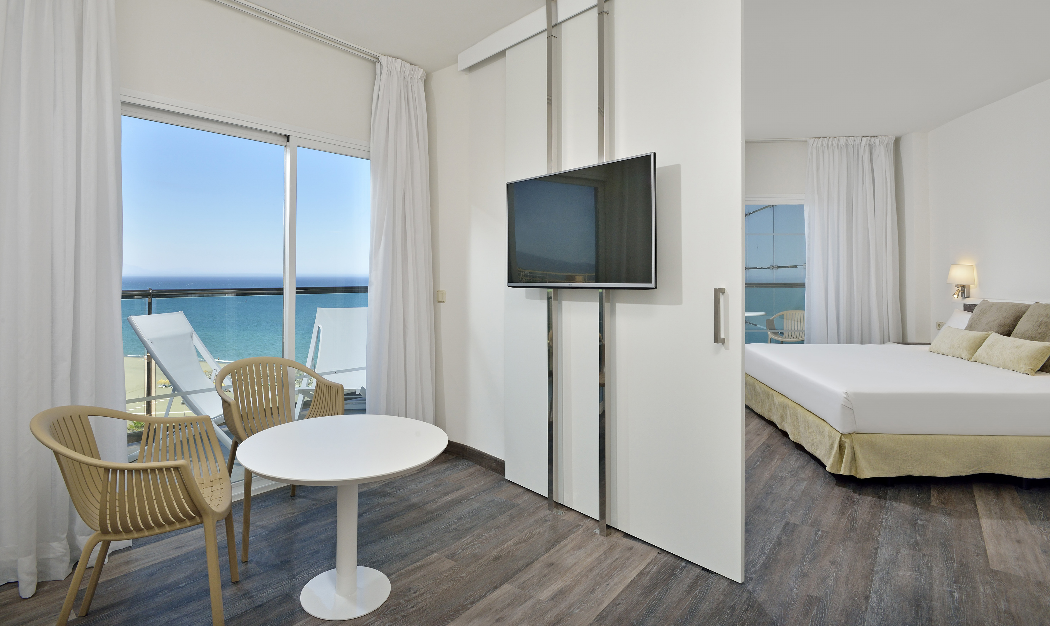 Modern hotel room with ocean view balcony, TV, and bedroom area.