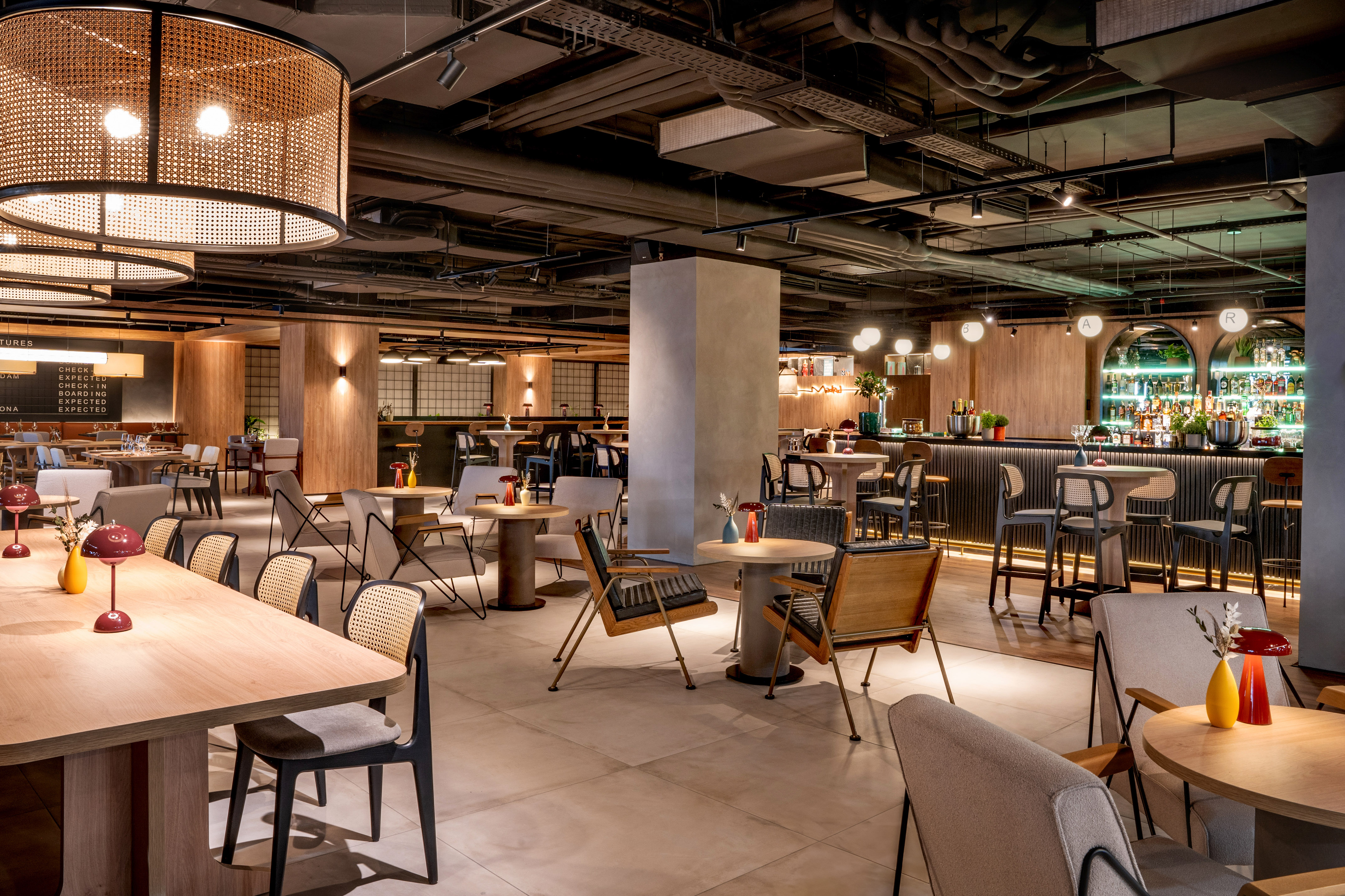 Modern hotel restaurant and bar with industrial ceiling and warm lighting.