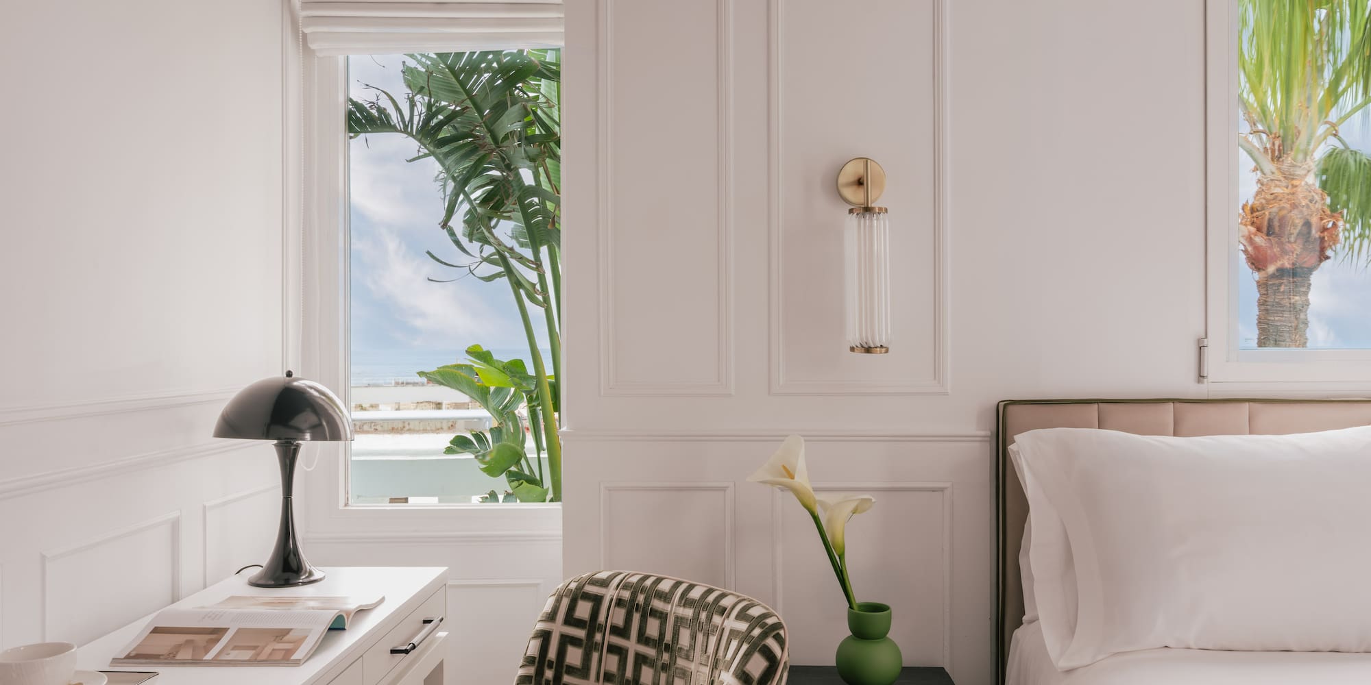 Modern bedroom: white decor, desk, bed, and windows with tropical palm trees.
