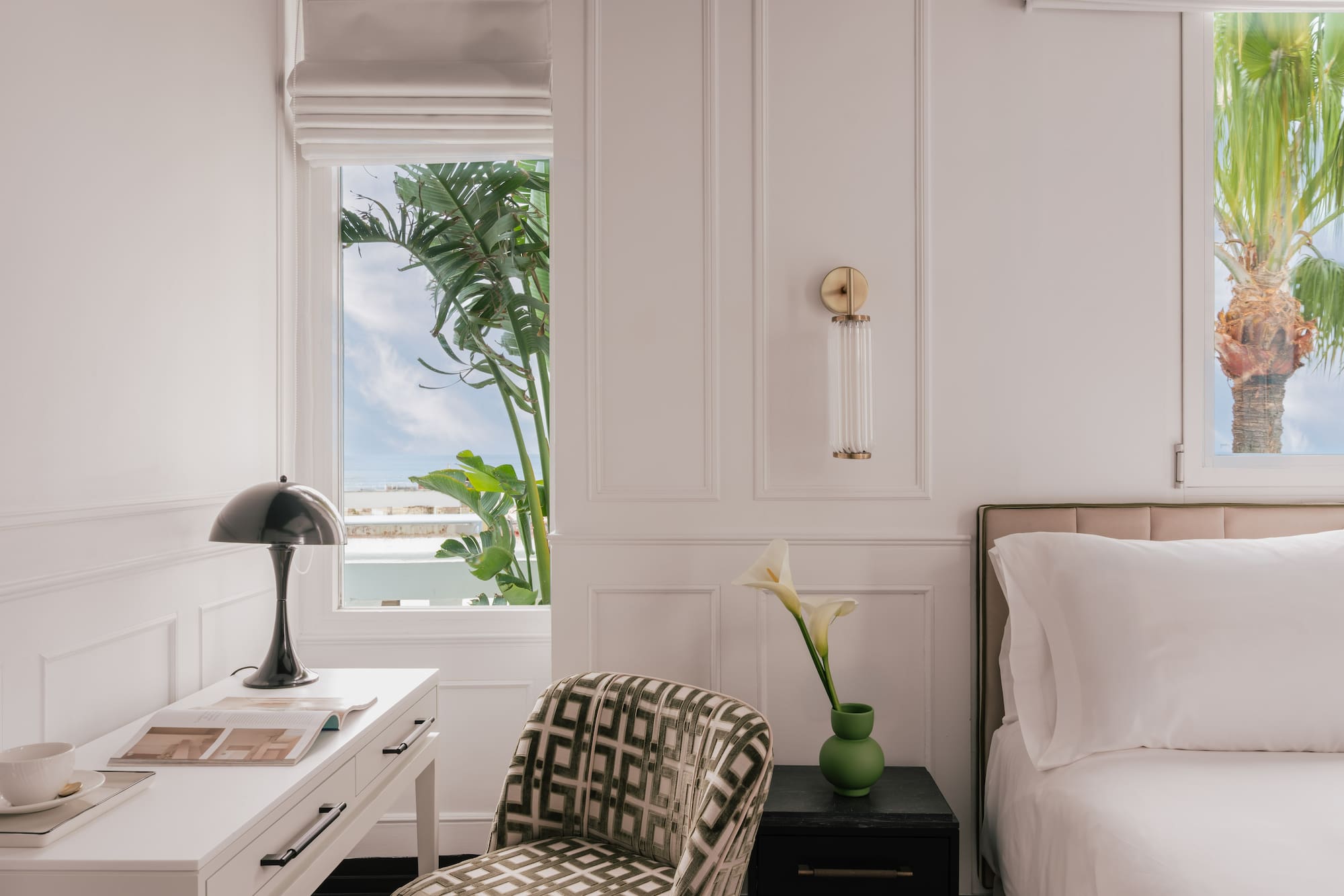 Modern bedroom: white decor, desk, bed, and windows with tropical palm trees.