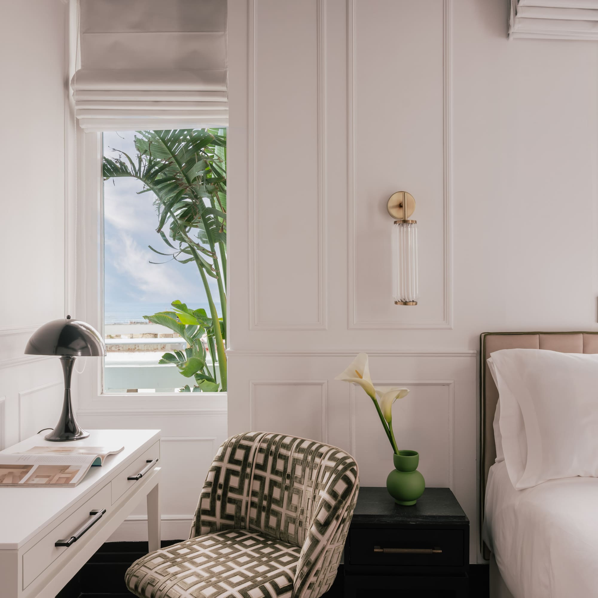 Modern bedroom: white decor, desk, bed, and windows with tropical palm trees.