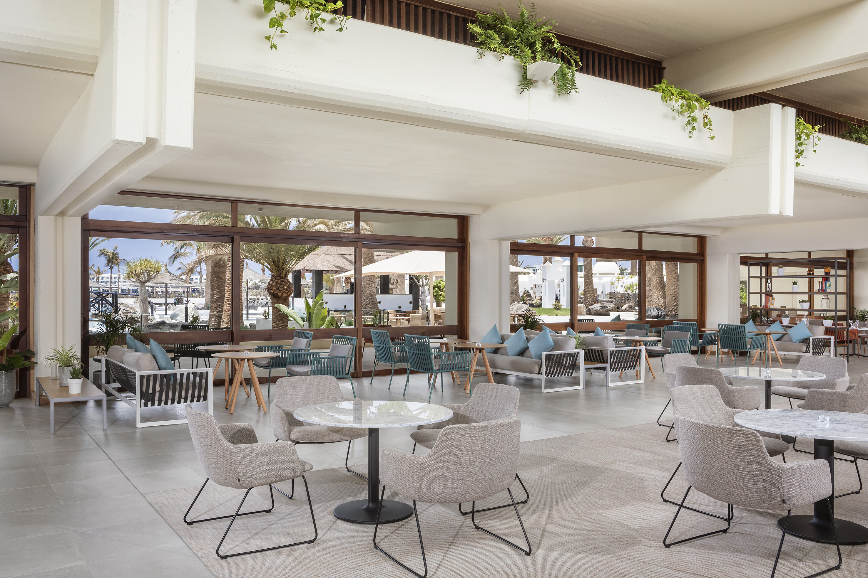 Bright modern hotel lounge with large windows, tropical view, and stylish seating.