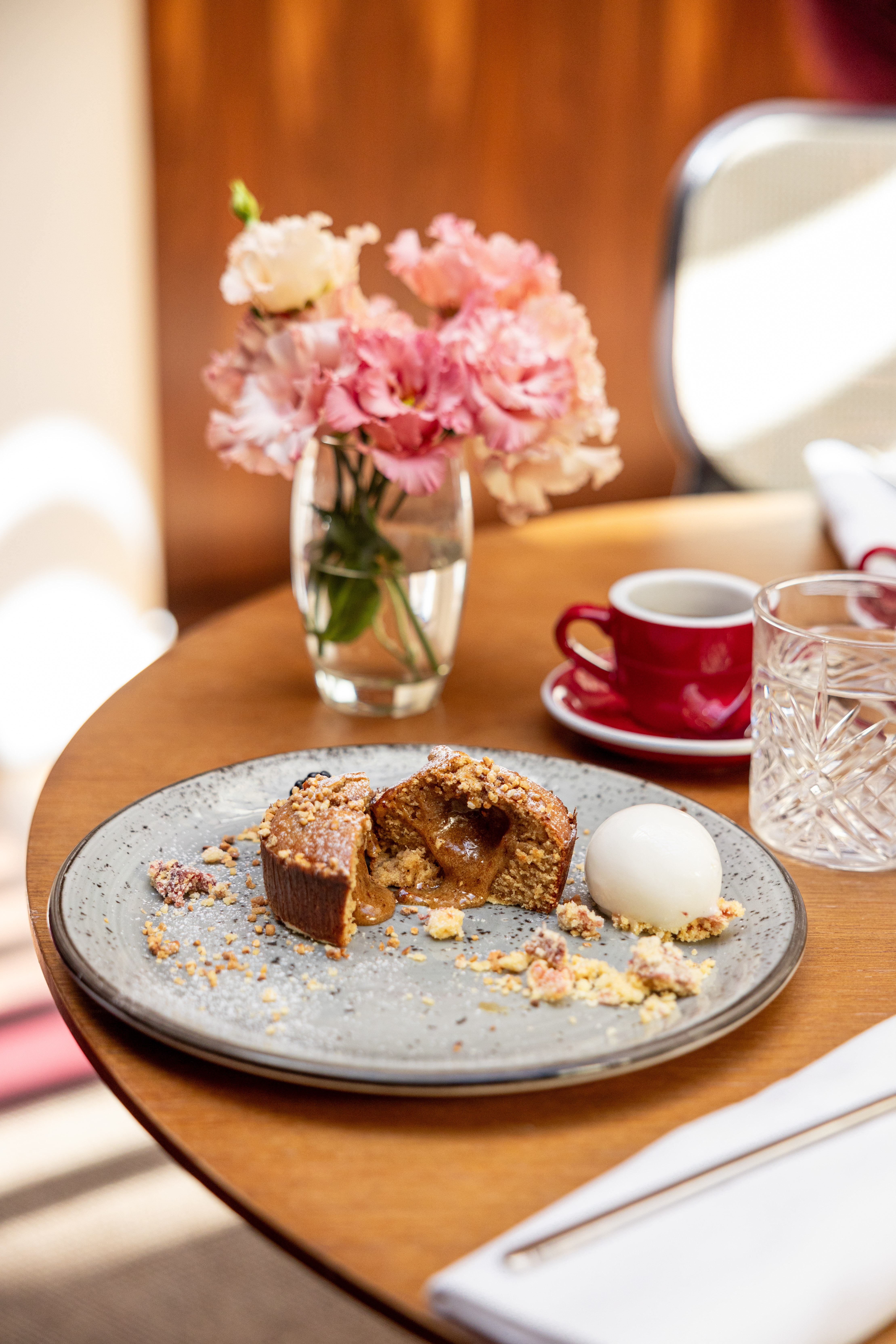 Molten caramel cake with nuts, ice cream, coffee, and pink flowers on table.