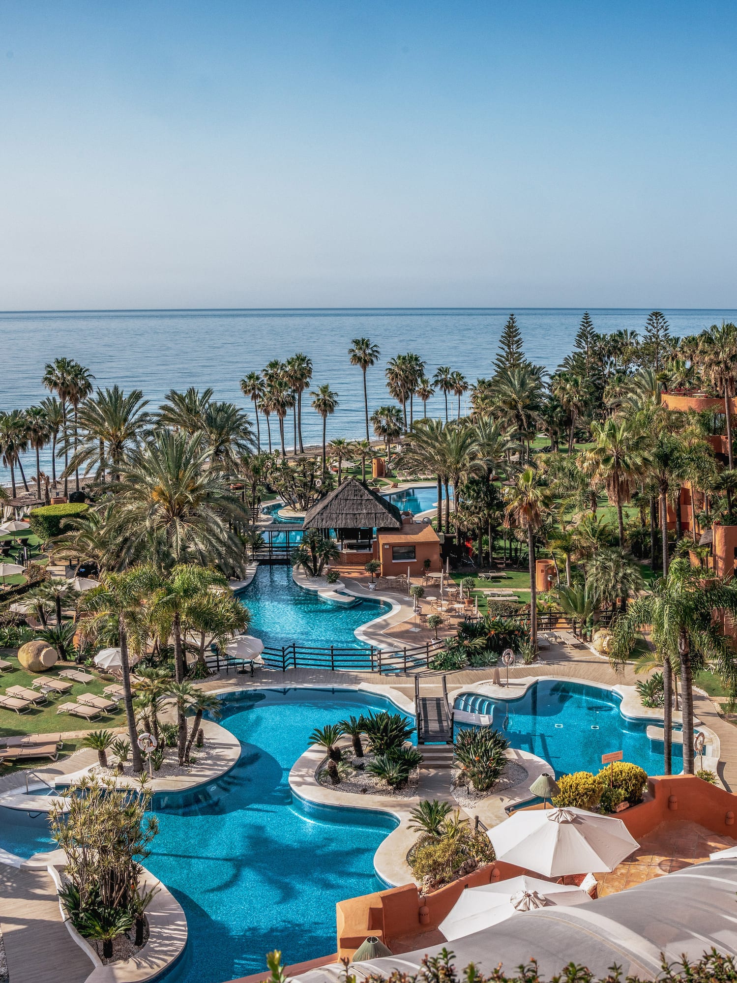 Luxury beachfront resort with multiple swimming pools, palm trees, and ocean view.