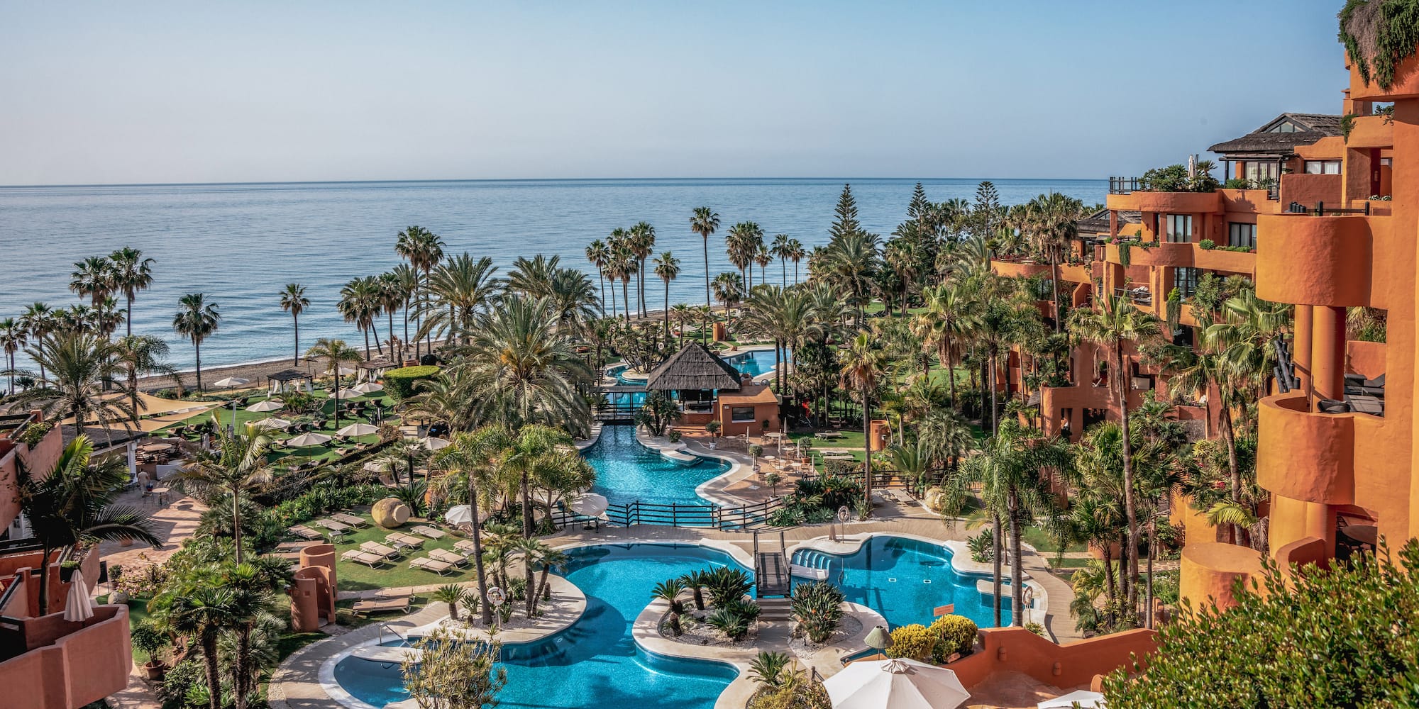 Luxury resort with winding blue pools, palm trees, and ocean view.